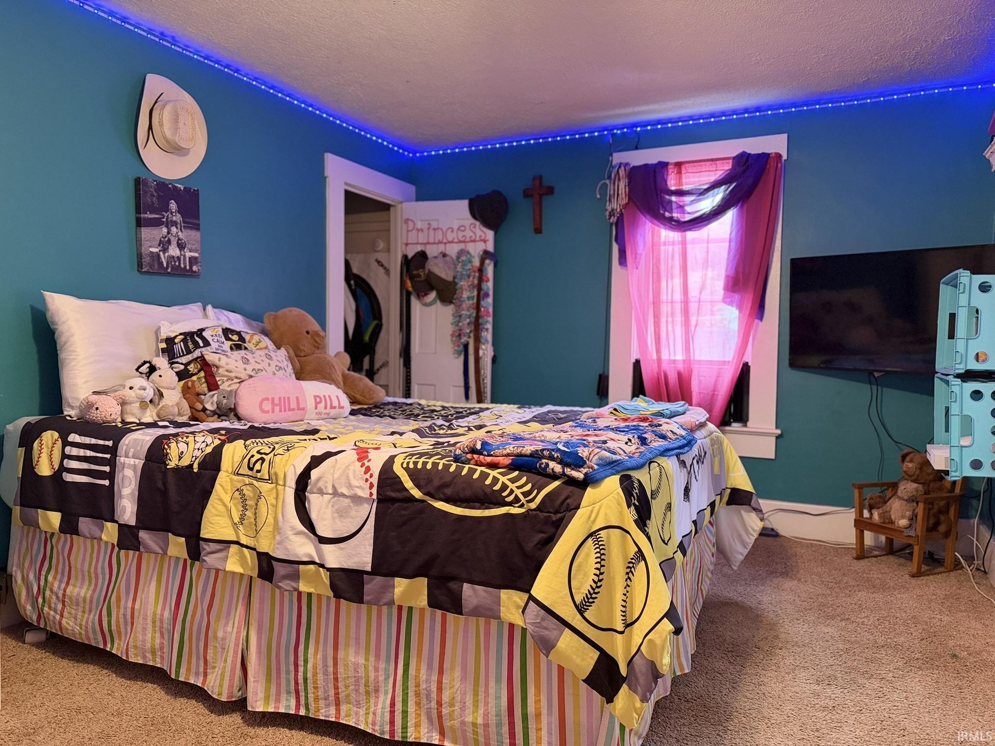Bedroom featuring blue accent walls, wall-mounted television, window with pink sheer curtains, and a closet with a white door frame