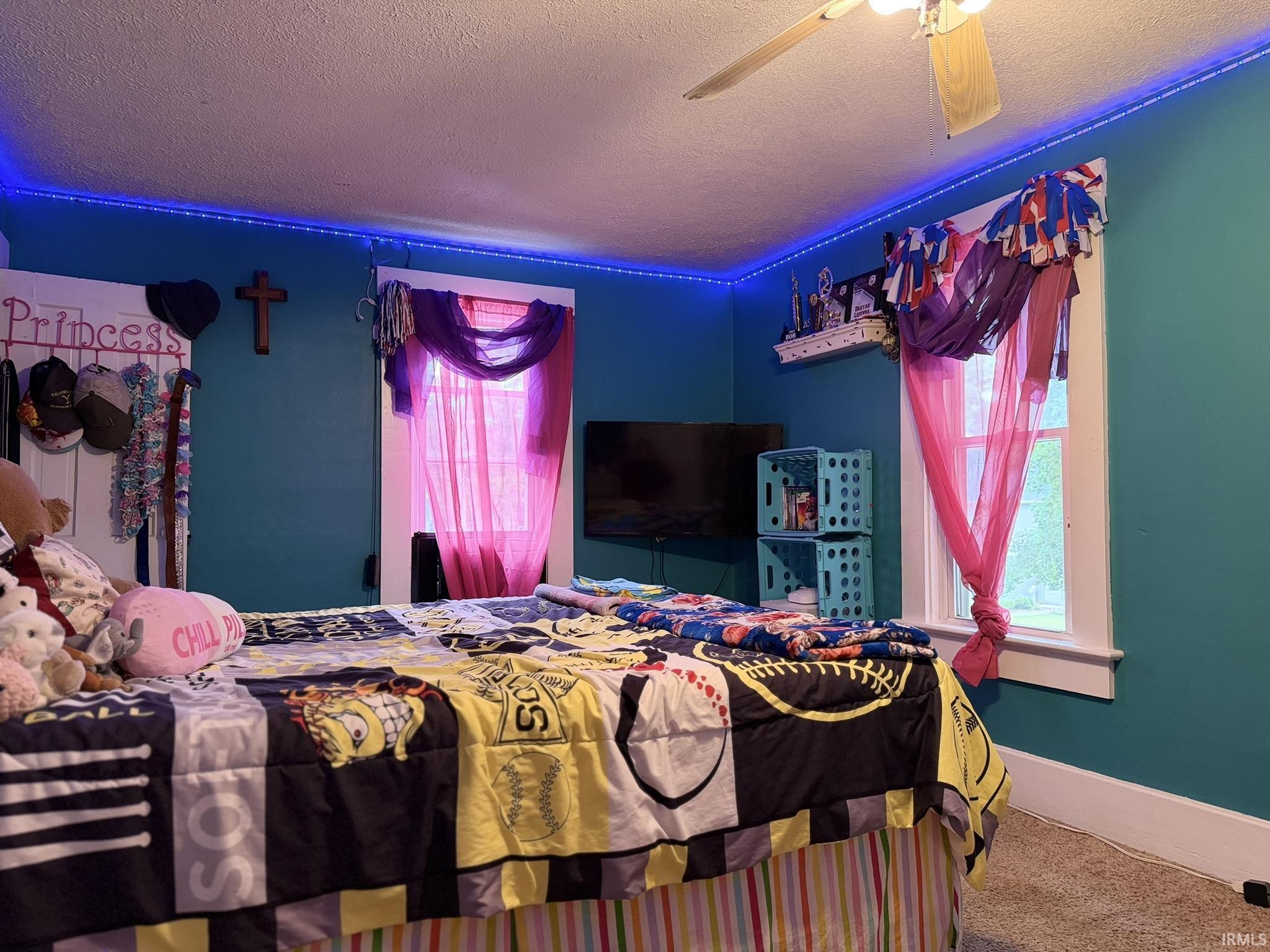 Interior room featuring a ceiling fan, two windows with white trim, and light-colored carpet flooring