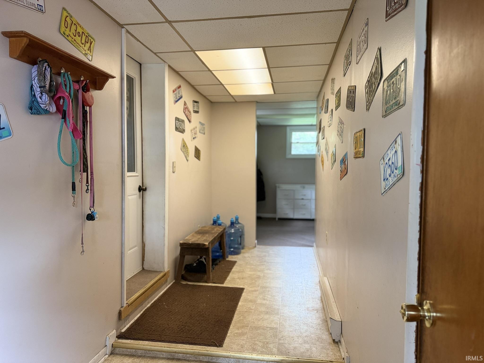 Hallway featuring light-toned flooring, drop ceiling with flush lighting, and a white paneled door