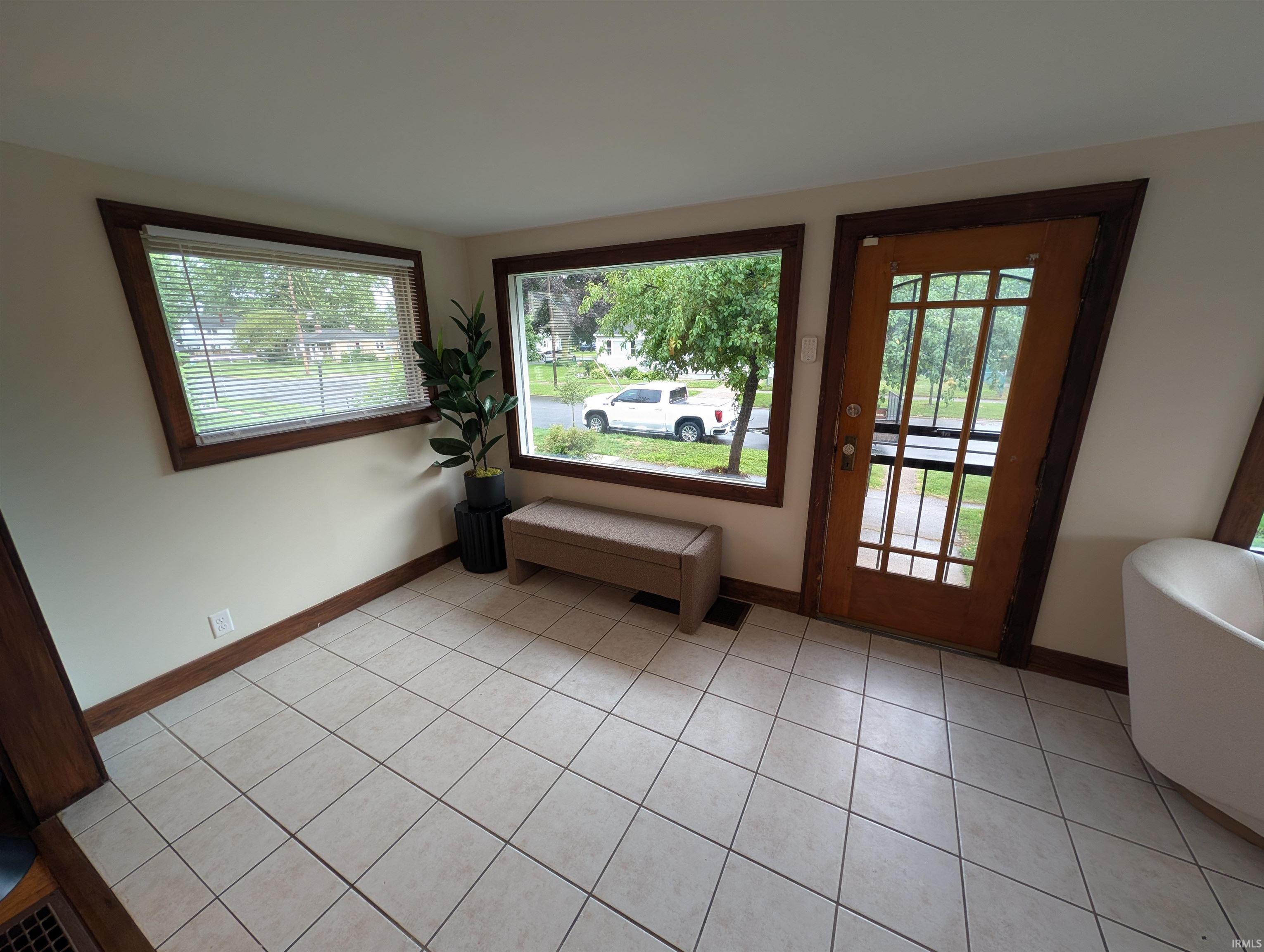 Entryway featuring light-toned tile flooring, two large windows with natural wood trim, and a wood-paneled door with glass inserts