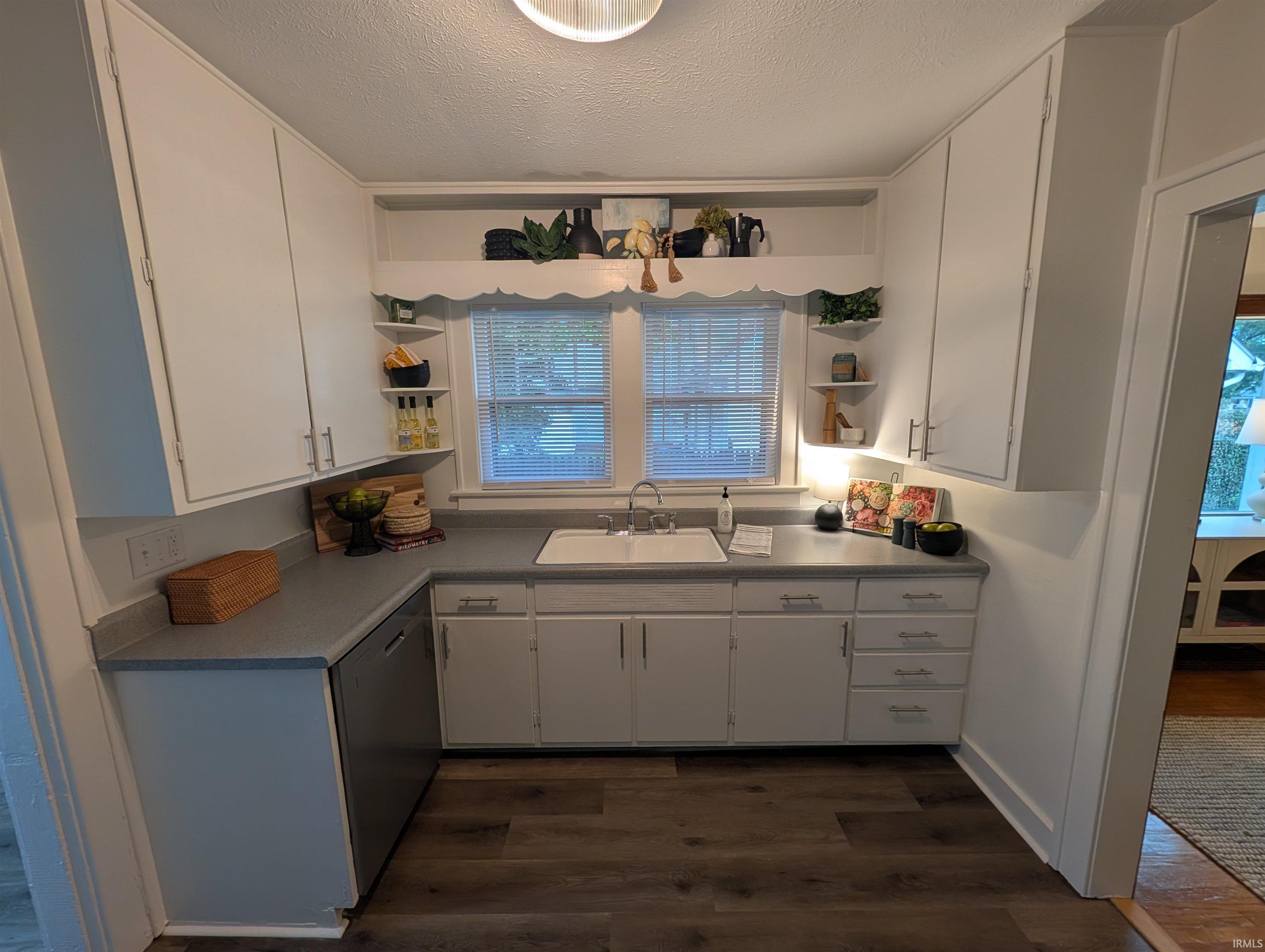 Kitchen featuring white cabinetry, wood-finish flooring, a stainless steel dishwasher, a single basin sink, and a countertop with integrated backsplash