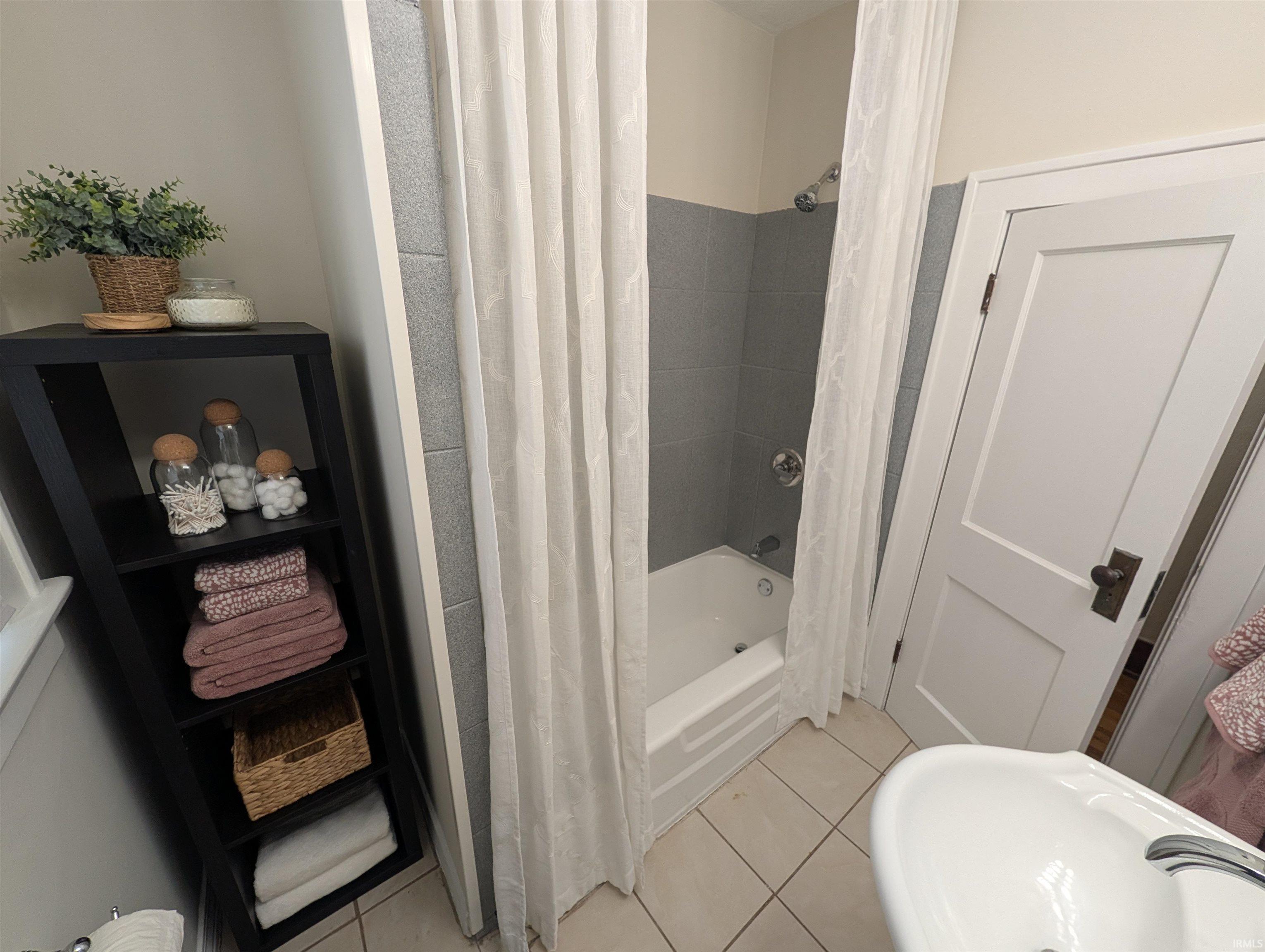 Bathroom featuring a white bathtub, gray tiled shower surround, and a white pedestal sink