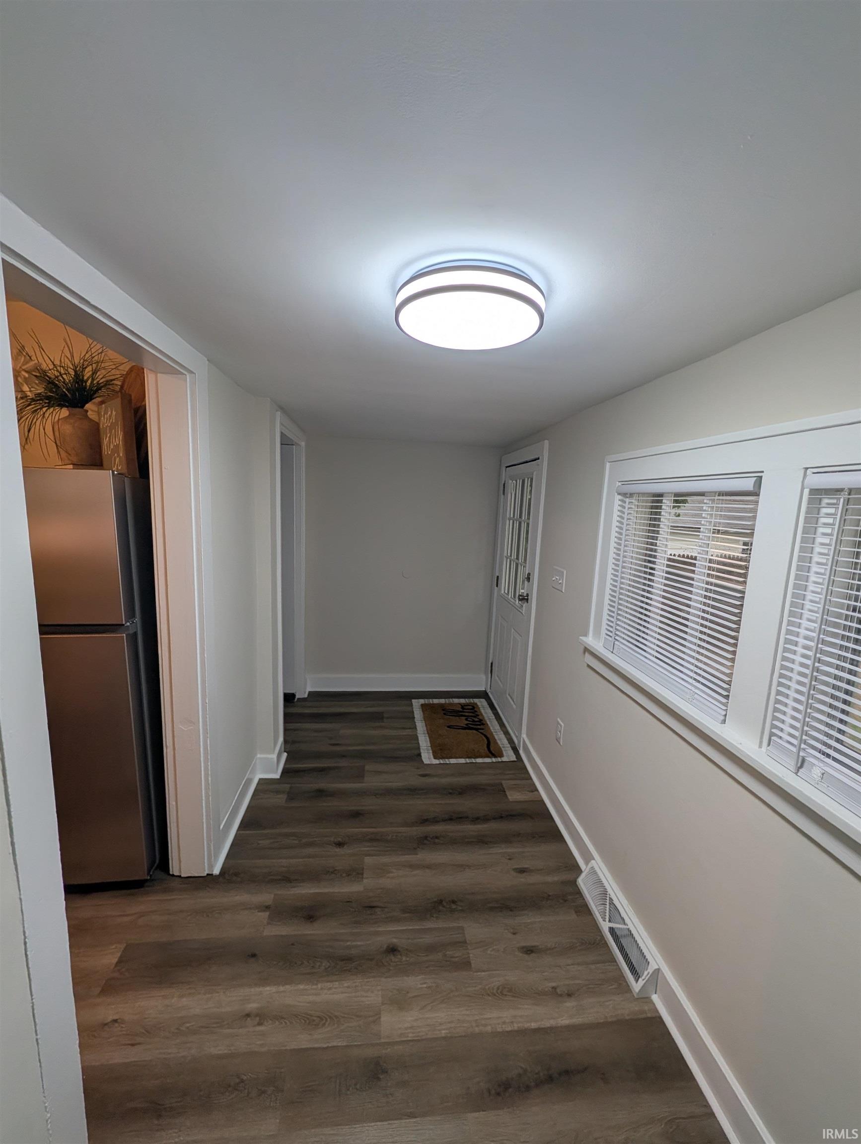 Hallway with wood-finish flooring, crisp white baseboards, and a modern flush-mount ceiling light