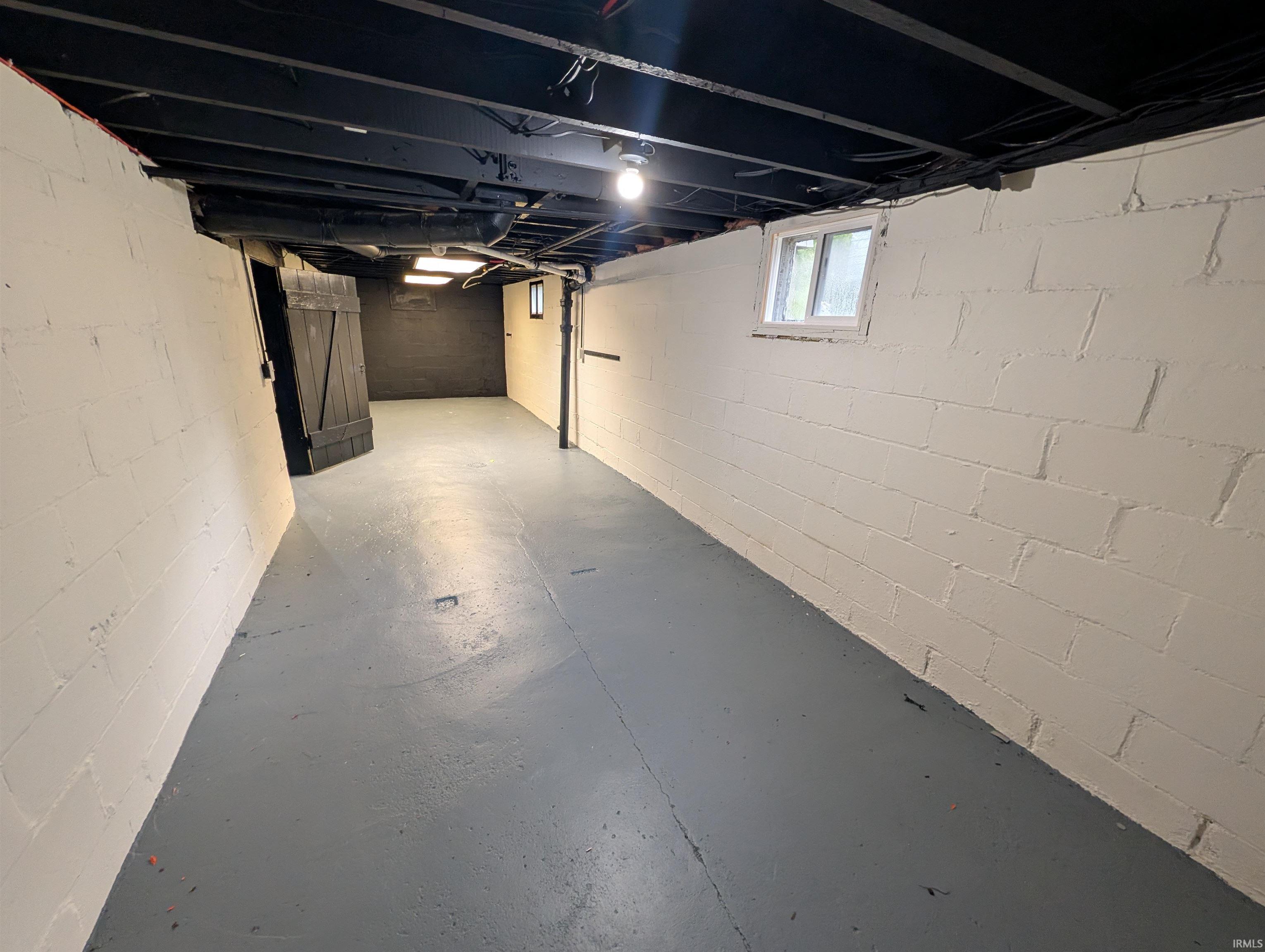 Spacious basement featuring painted concrete block walls, exposed ceiling joists painted black, and a grey painted concrete floor