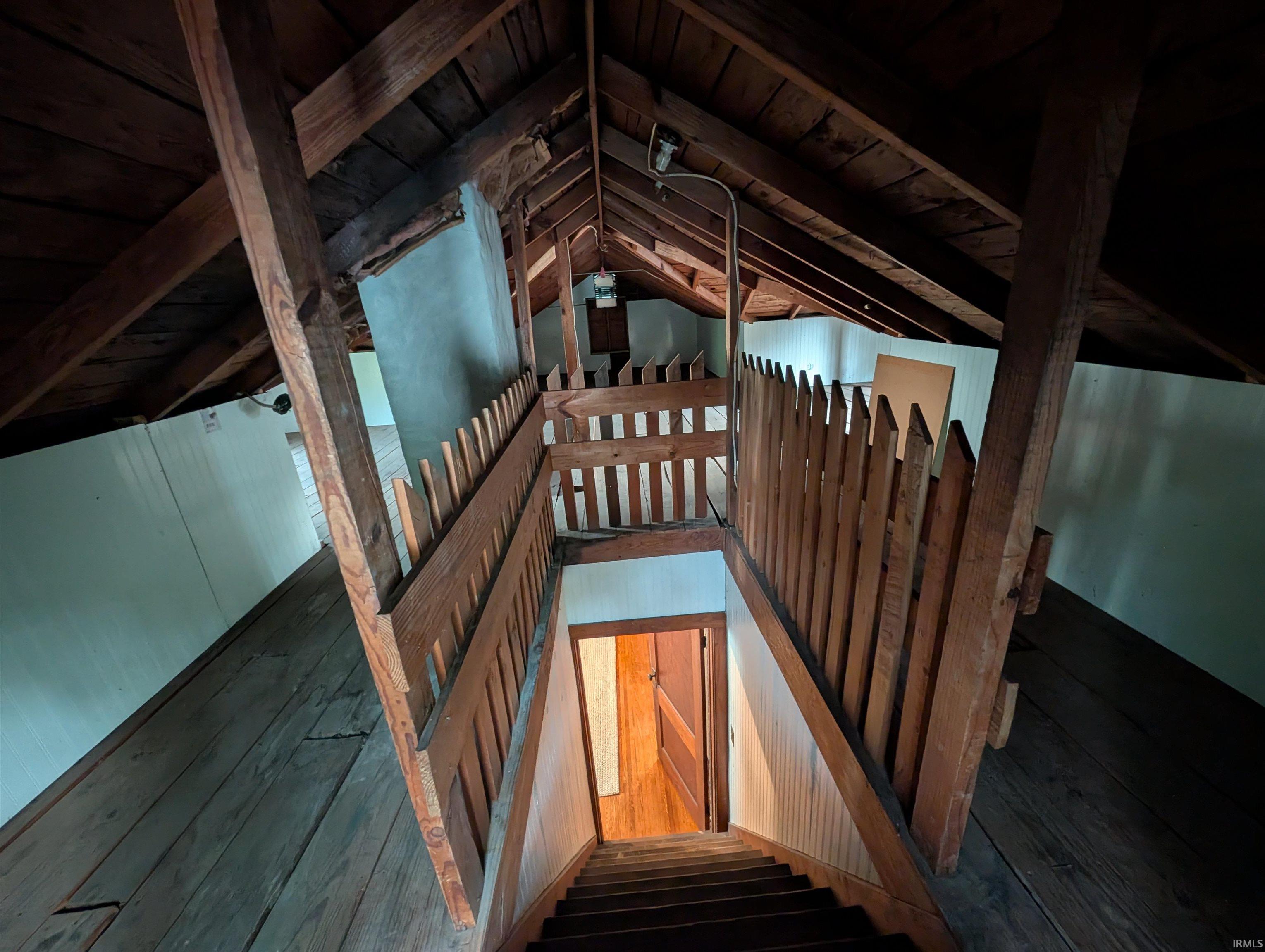 Attic space featuring exposed wood beams, wood flooring, and a wood staircase with picket-style railing