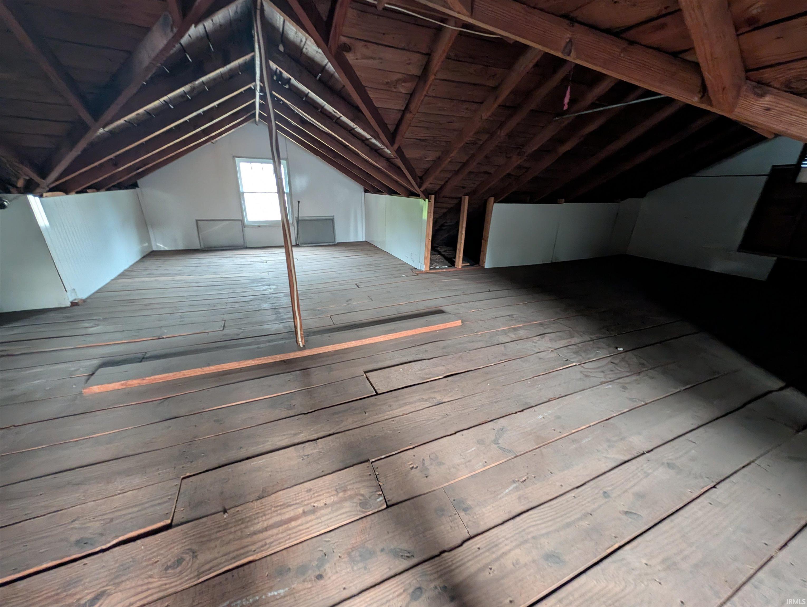 Spacious attic space featuring exposed wood rafter ceilings and wood plank flooring