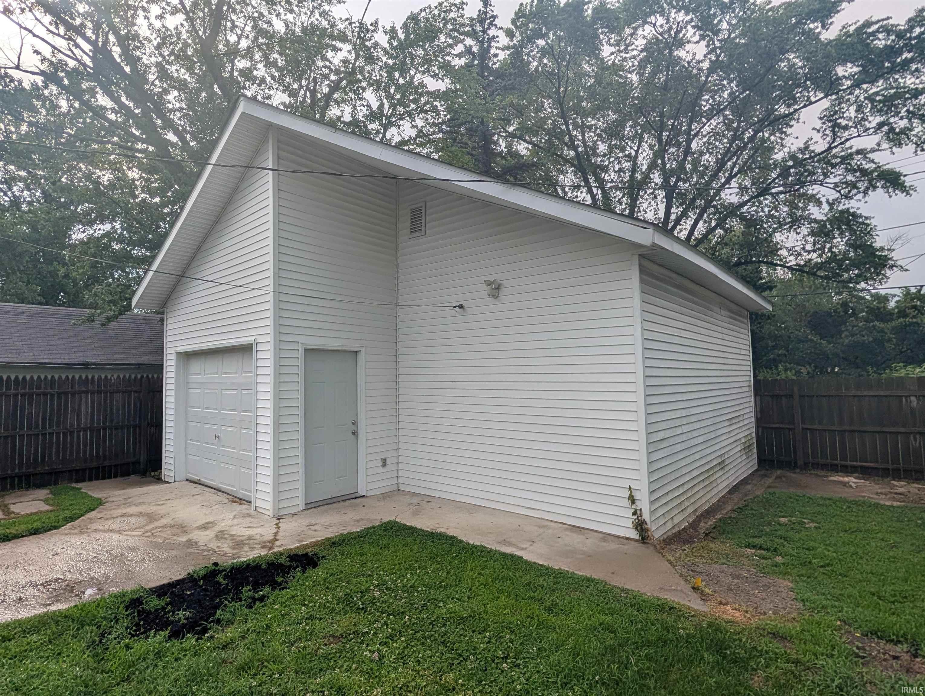 Detached garage featuring white vinyl siding, a single garage door, and a side entry door