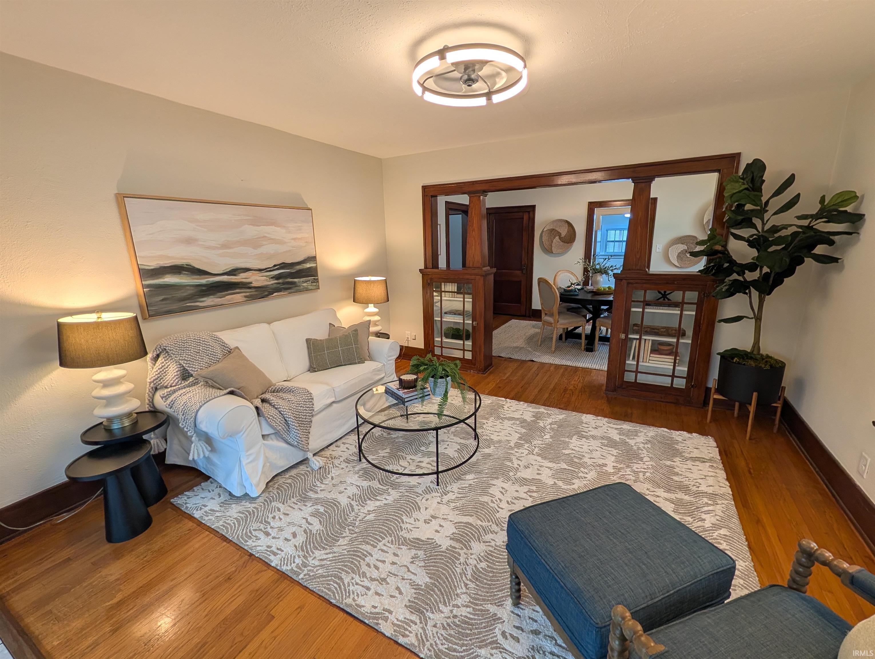 Living room featuring wood-finish flooring, a modern circular ceiling light fixture, and an open entryway with built-in wooden cabinetry framing the opening