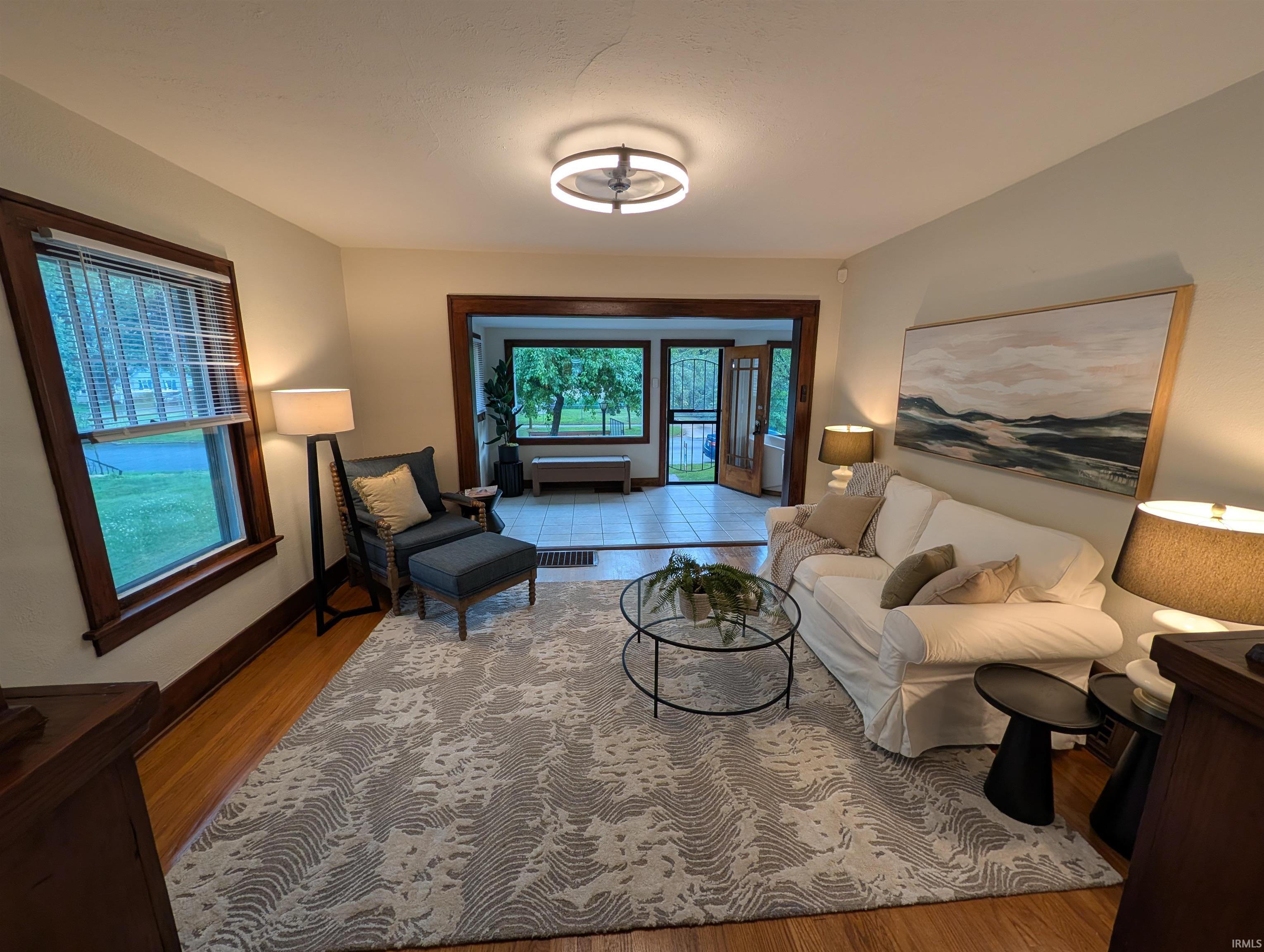 Living area featuring wood-finish flooring, a contemporary ceiling fixture, and a wide entryway to an additional room