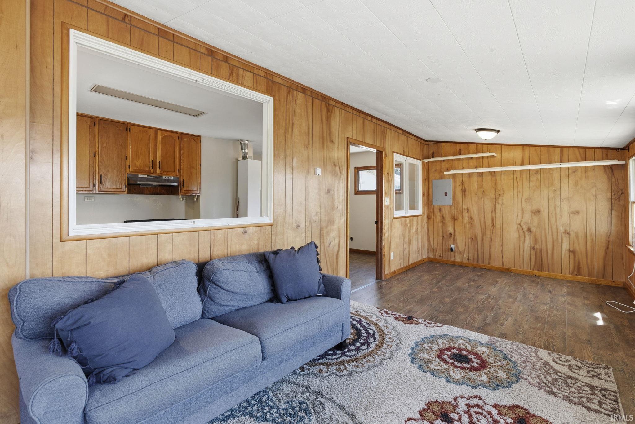 Living area featuring wood paneling, wood-finish flooring, and a pass-through window to the kitchen