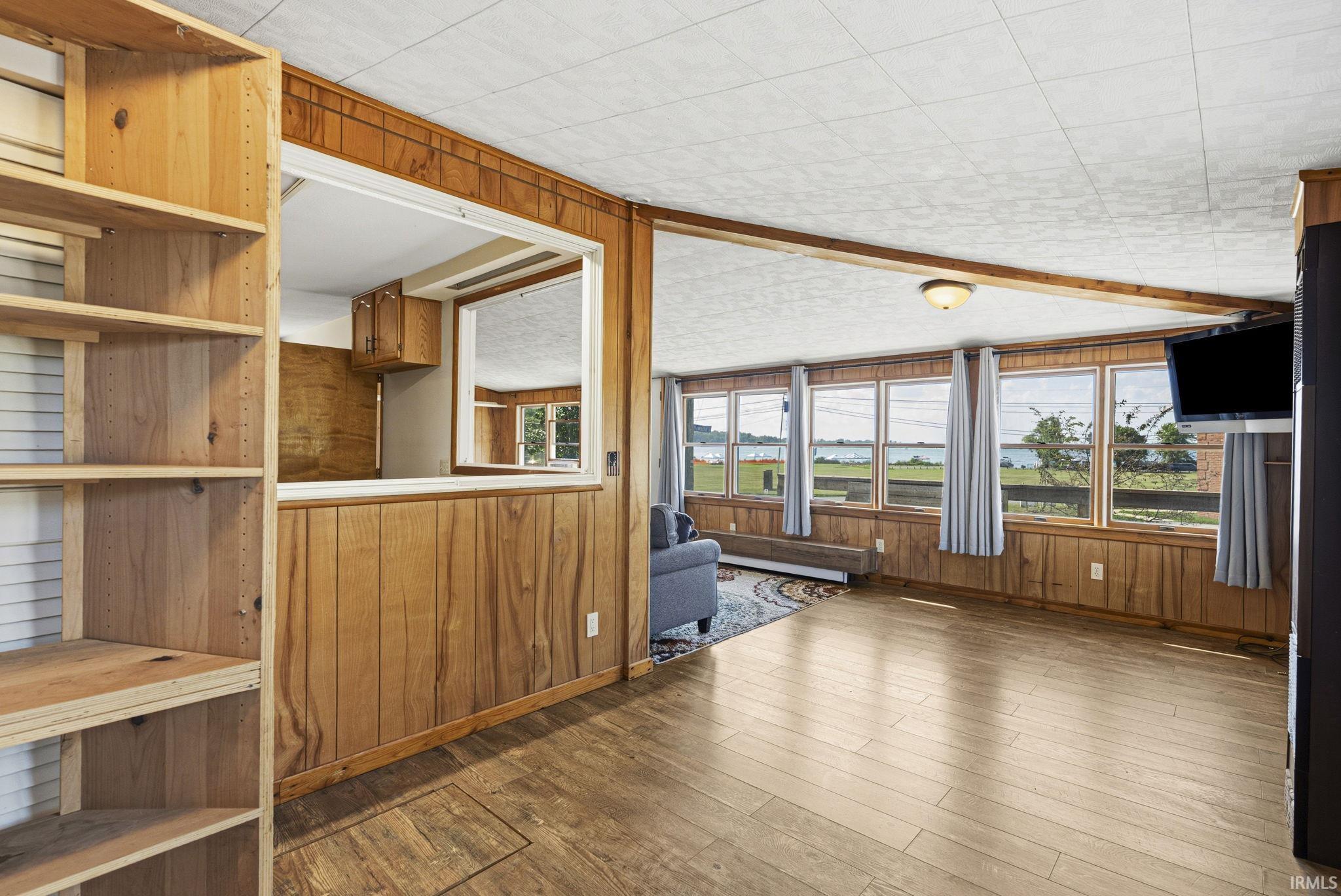 Open-concept living area featuring wood-finish flooring, wood paneling, built-in shelving, and multiple windows with water scenery
