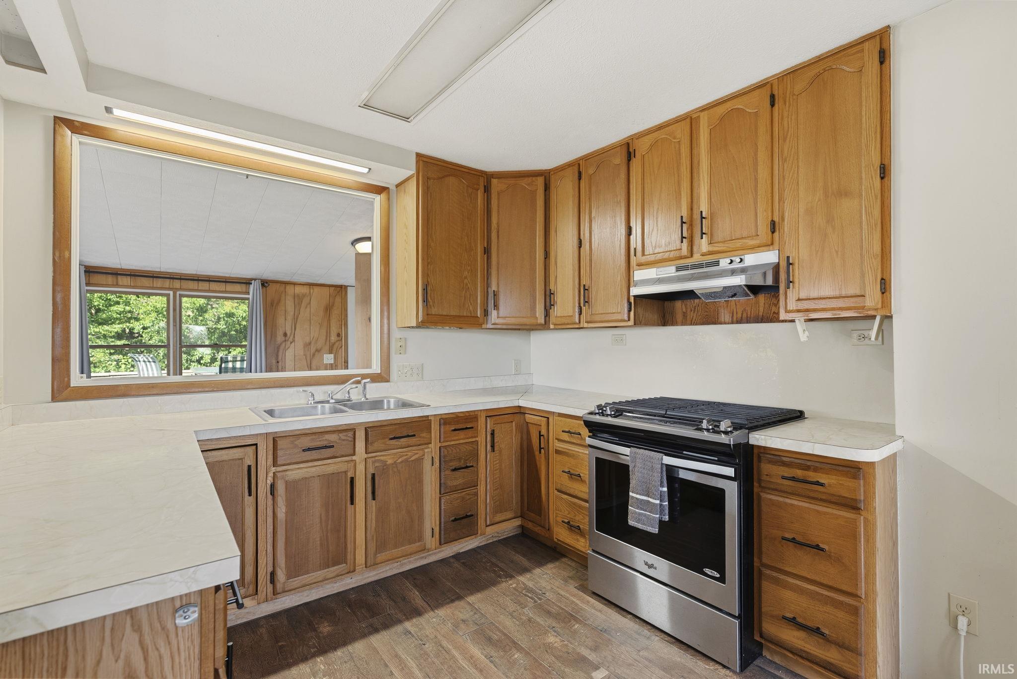 Kitchen featuring wood-finish cabinetry, light-toned countertops, a stainless steel range, and a double basin sink