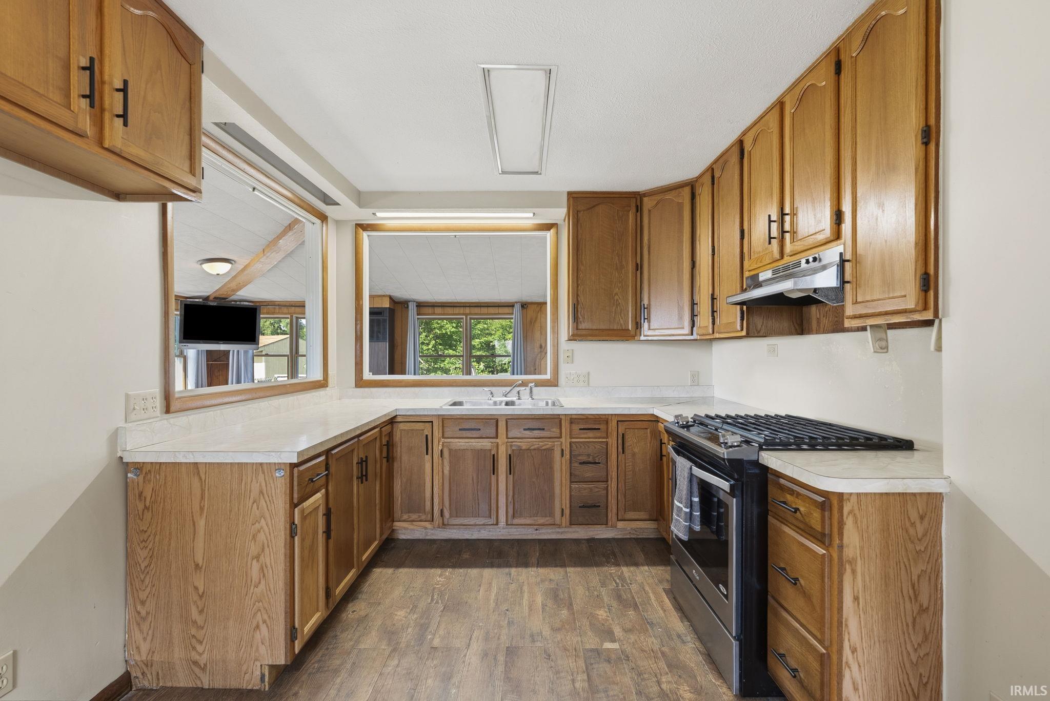 U-shaped kitchen featuring wood cabinetry with dark hardware, white countertops, a stainless steel range with overhead hood, and wood-finish flooring