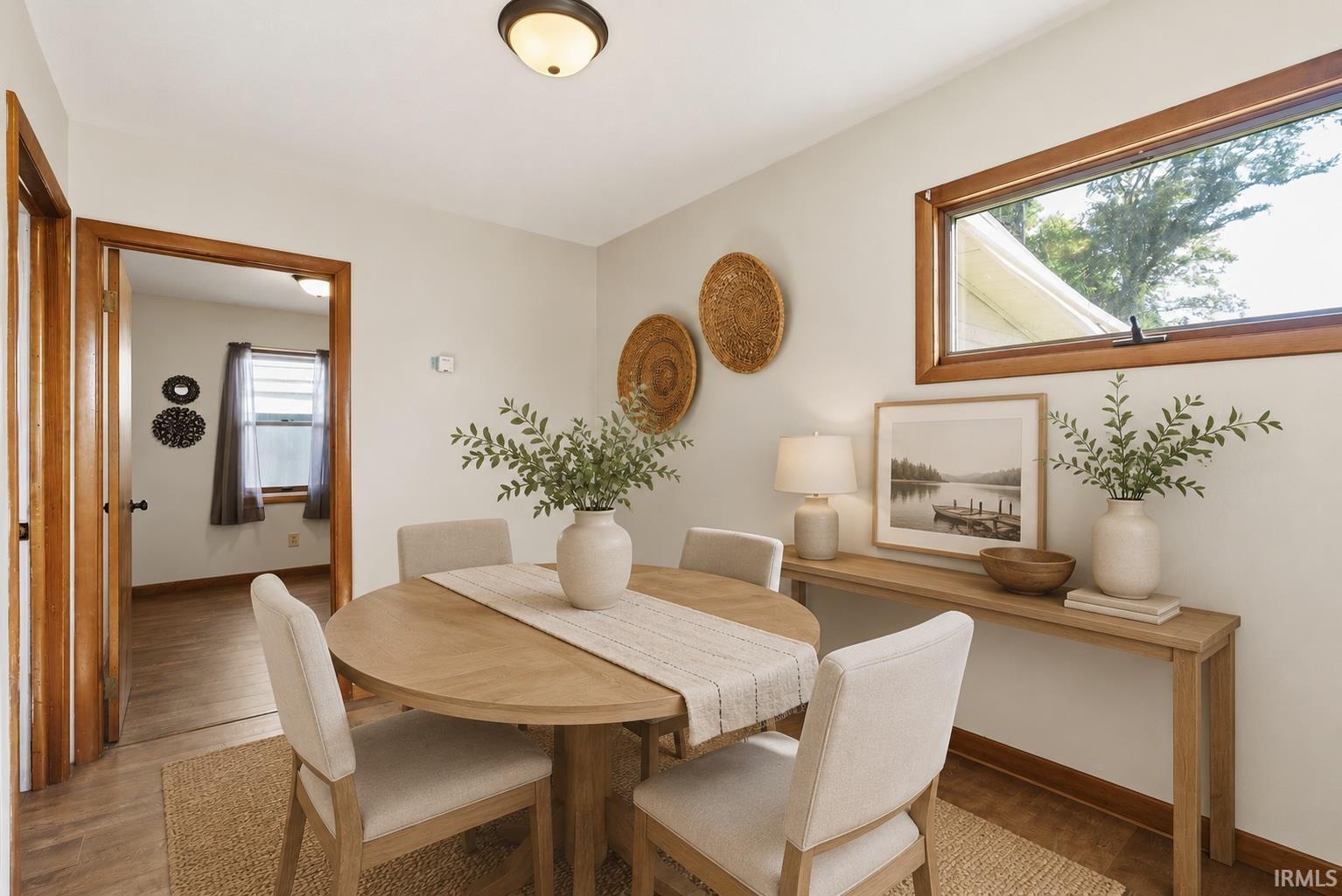 Dining area featuring light wood-finish flooring, a wood-trimmed window, a ceiling-mounted light fixture, and a wide entryway with wood trim