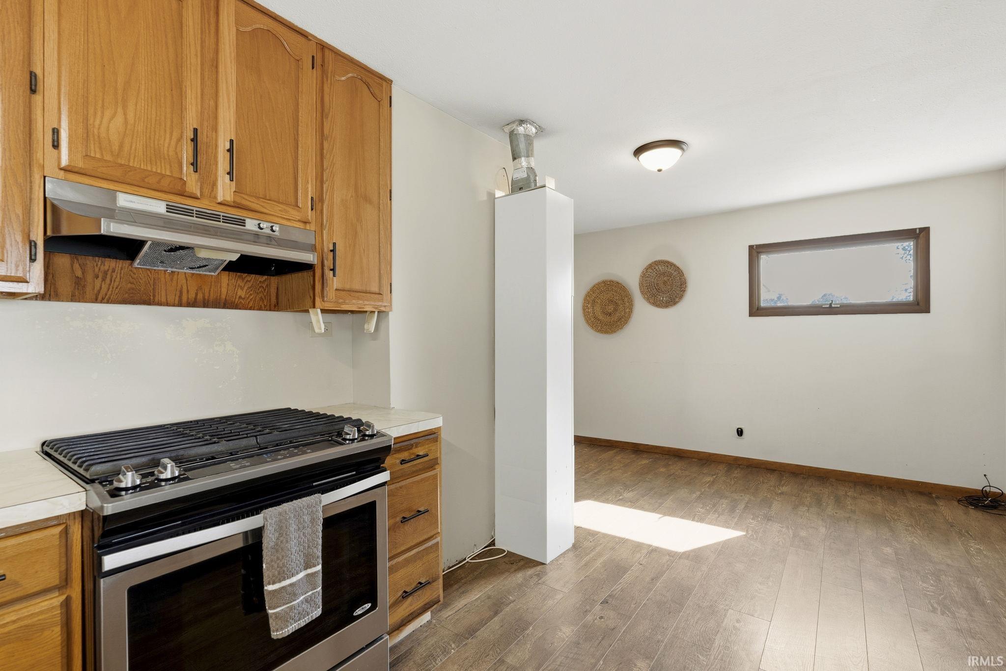 Kitchen area featuring light wood cabinetry, stainless steel range with overhead ventilation, and light-toned countertops