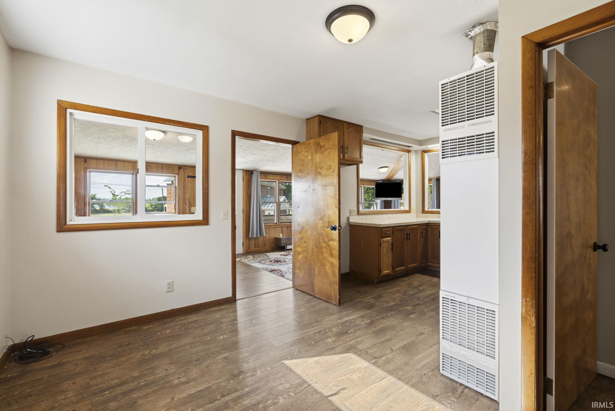 Interior space featuring wood-finish flooring, a wall-mounted heating unit, and a pass-through window with wood trim