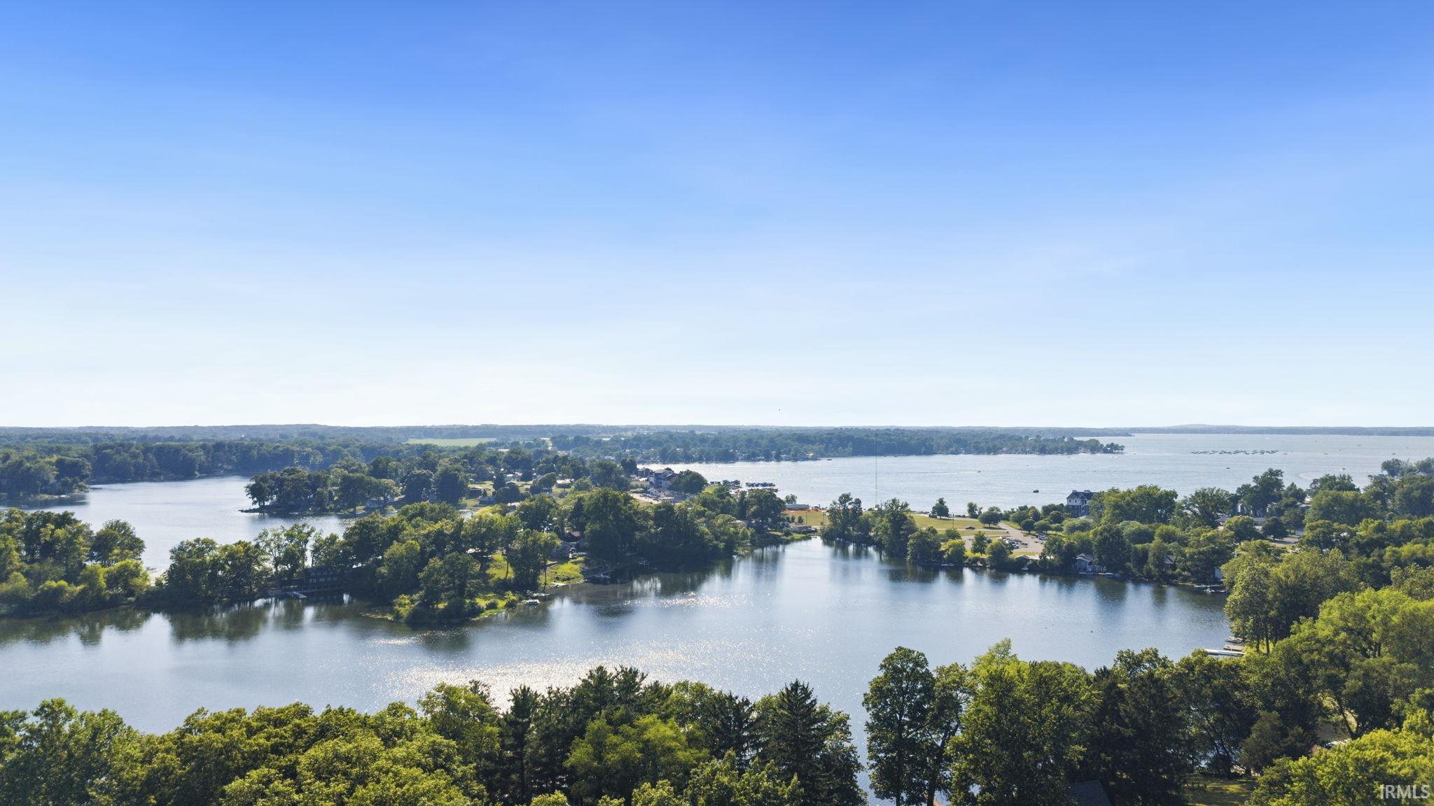 Expansive aerial perspective showcasing a lakefront property with surrounding water features and lush green trees
