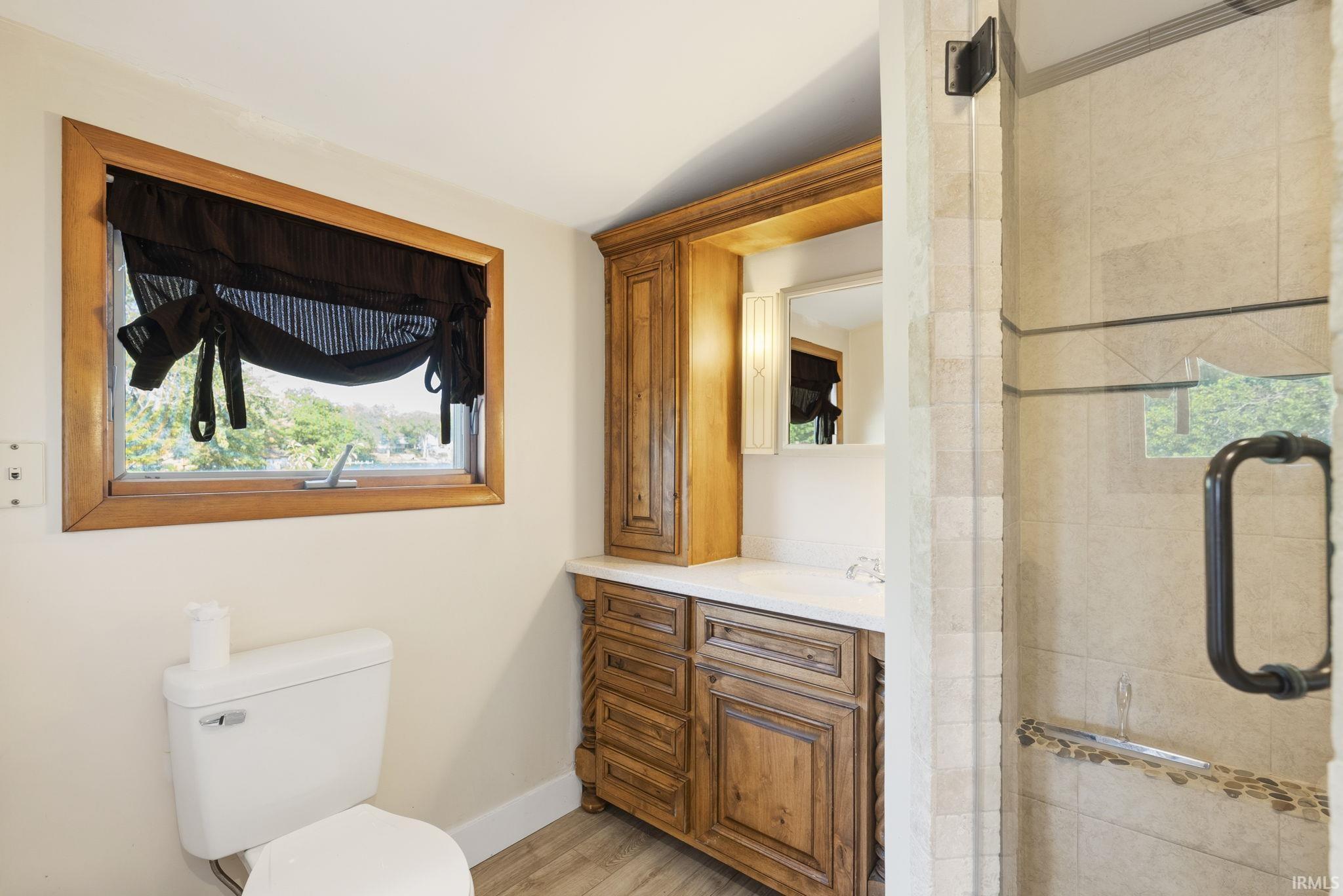 Bathroom featuring a wood-framed window, vanity with a wood-finish cabinet and solid surface countertop, and a glass-enclosed shower with tiled walls and stone accent strip