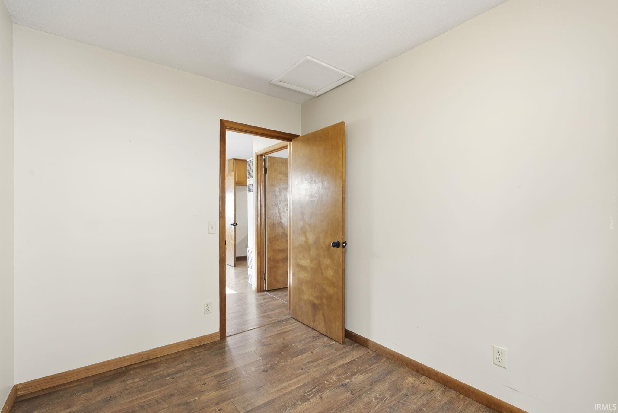 Interior room featuring wood-finish flooring, light-toned walls, and a wooden door with a black doorknob
