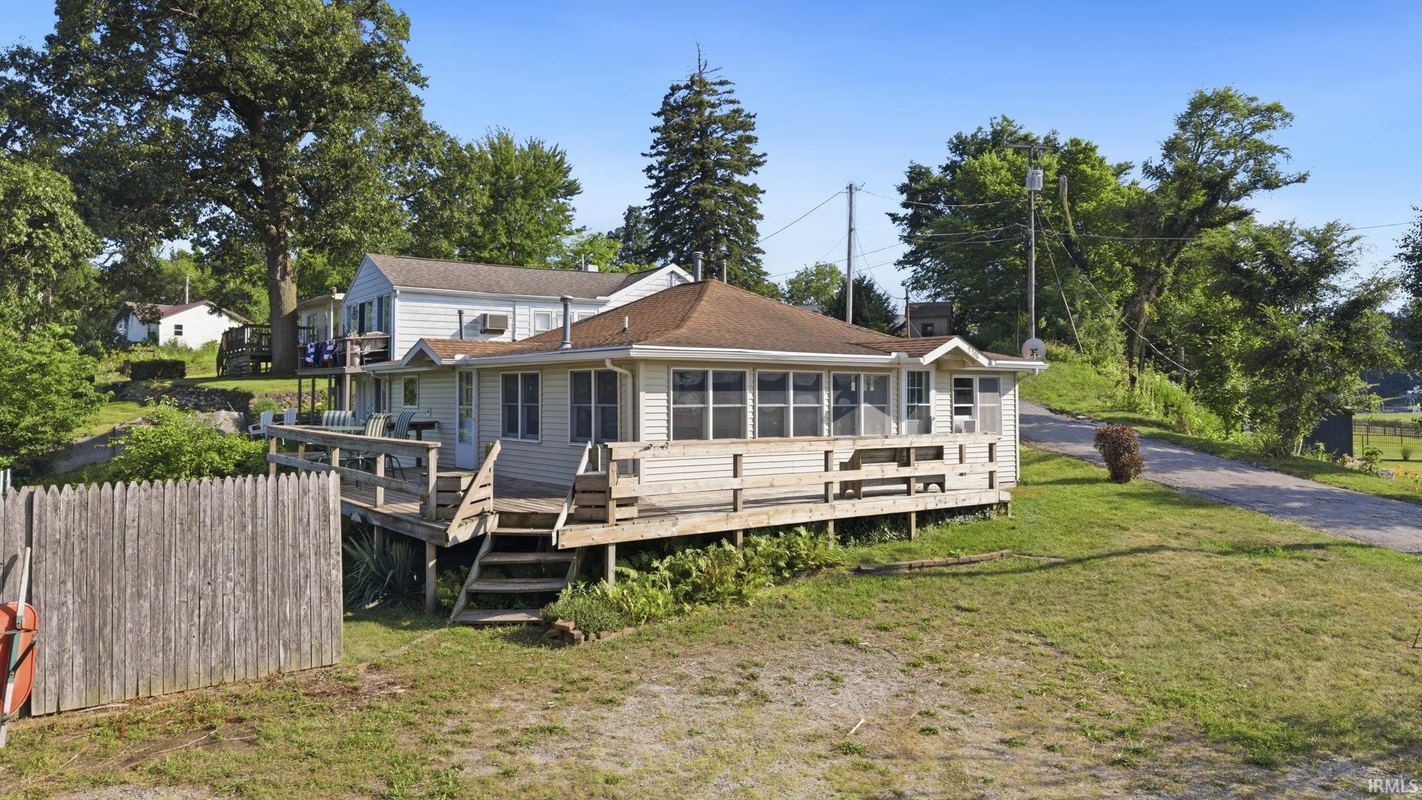 Residential structure featuring a wrap-around elevated deck, multiple windows, and a partially enclosed porch