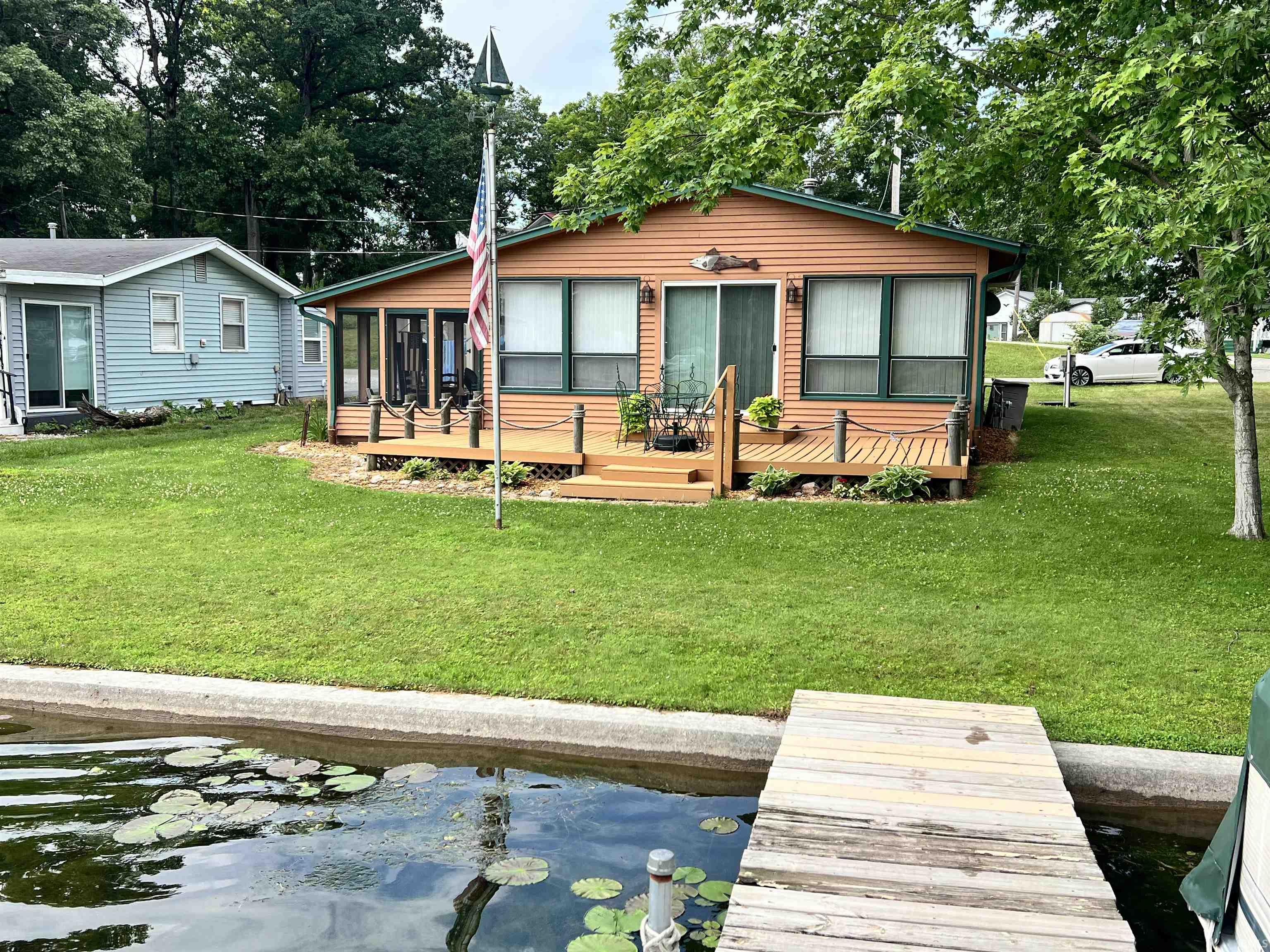 Waterfront property featuring a wooden dock, concrete seawall, and a spacious green lawn