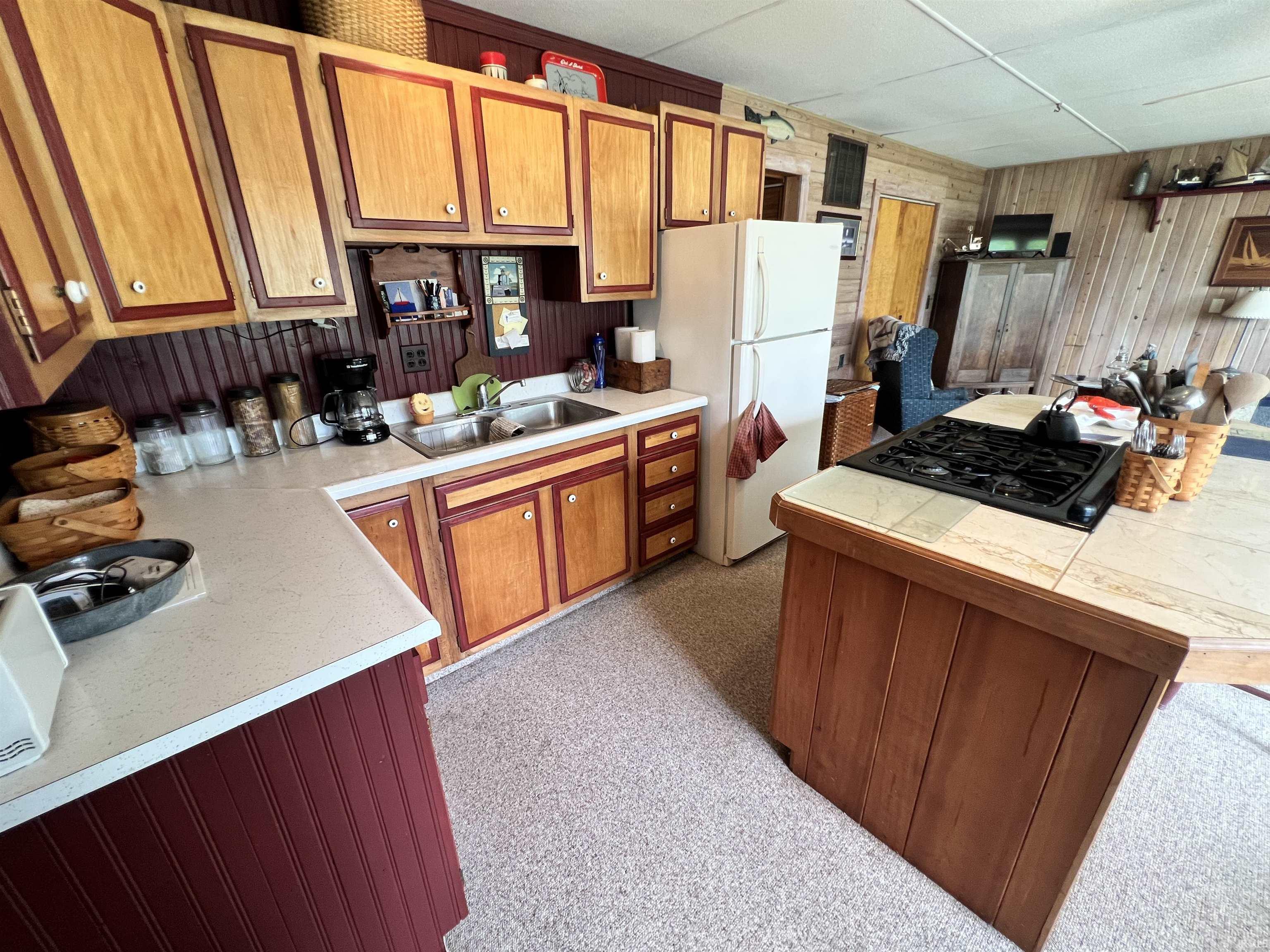 Kitchen featuring wood-finish cabinetry with red trim, a double basin stainless steel sink, and light-toned countertops