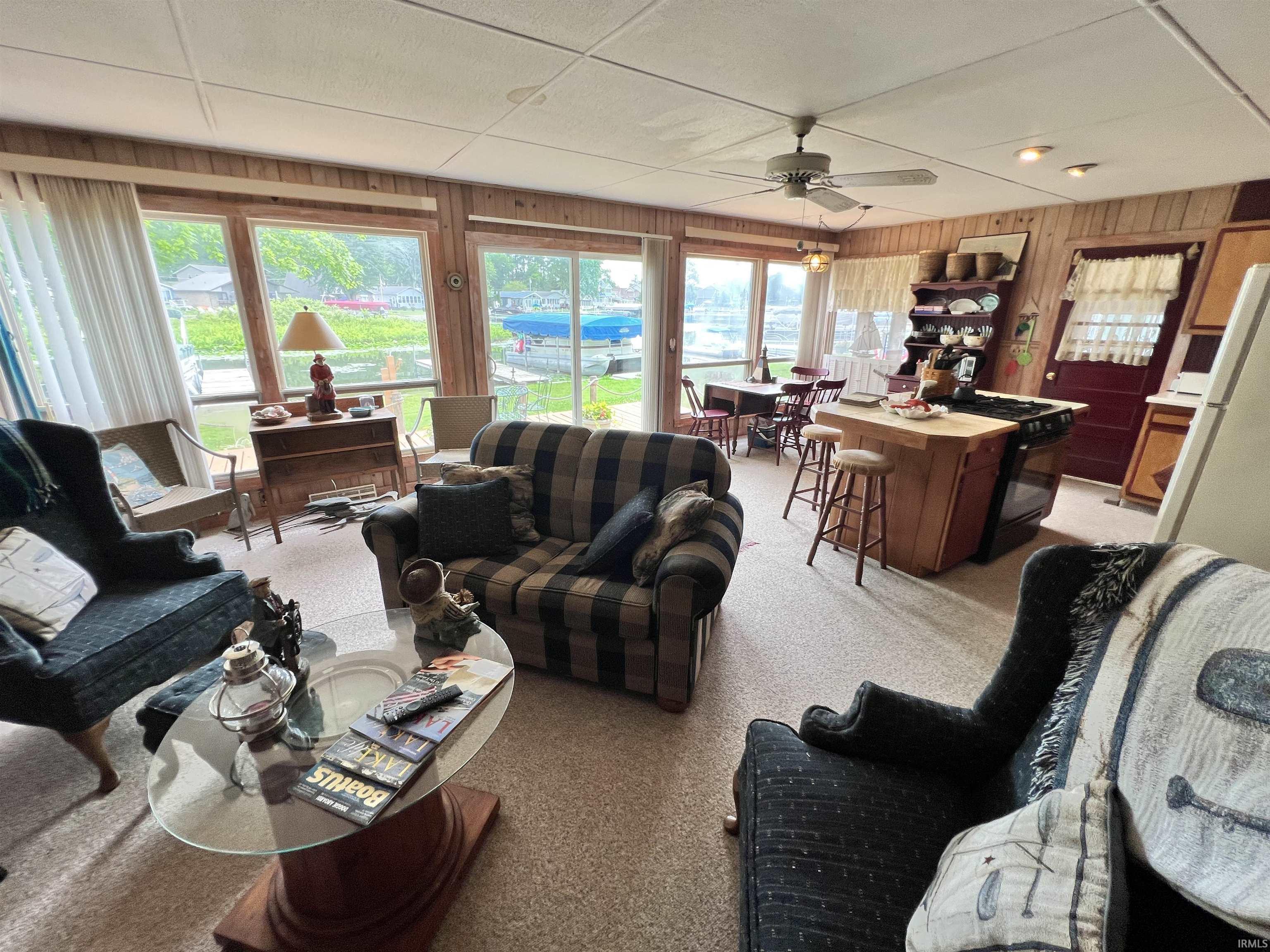 Open-concept living space featuring wood paneling, extensive window line, and a ceiling fan