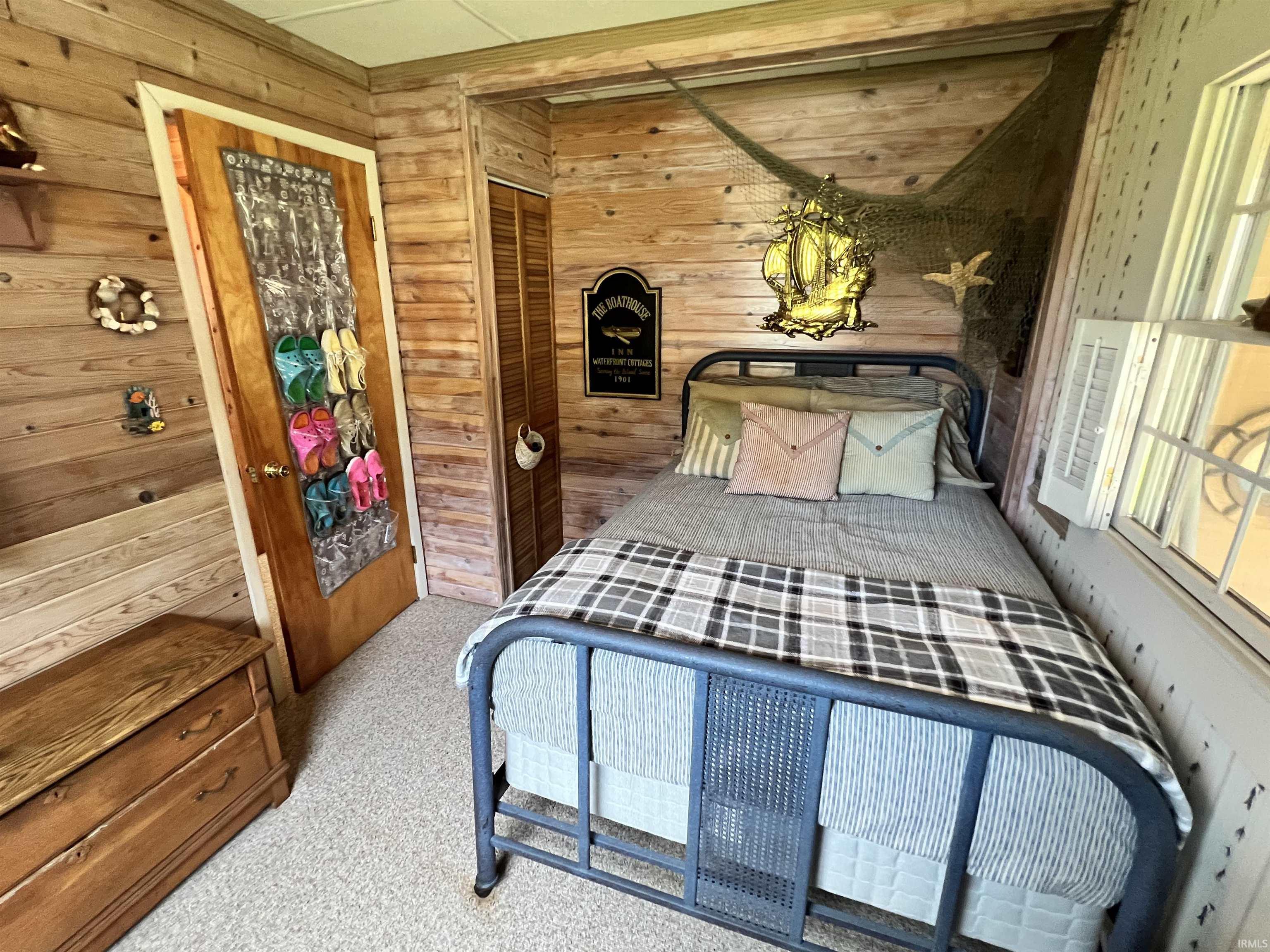 Wood-paneled room featuring a metal bed frame, window, and wood-finish door