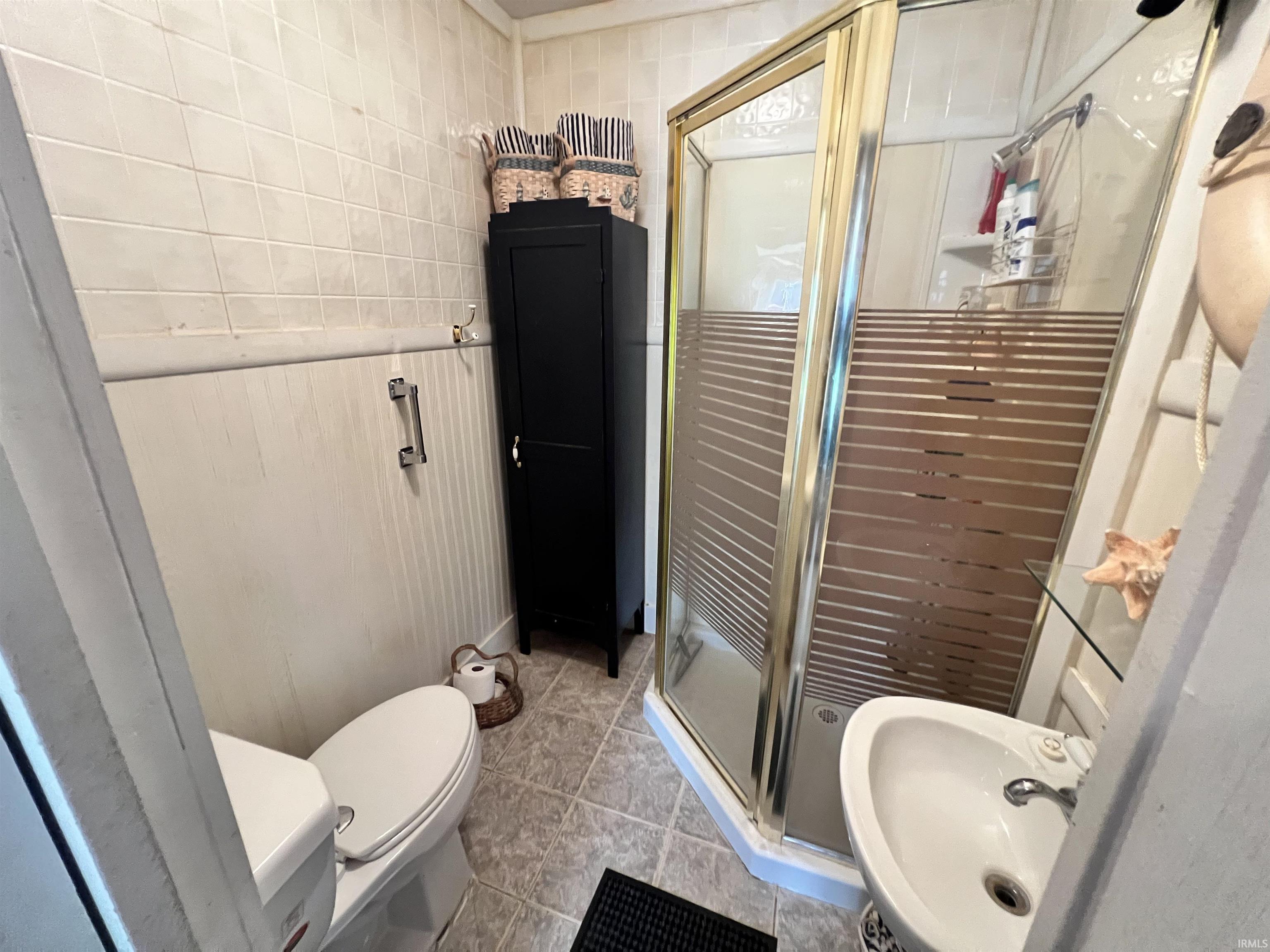 Compact bathroom featuring a corner shower with a gold-toned frame and privacy-striped glass