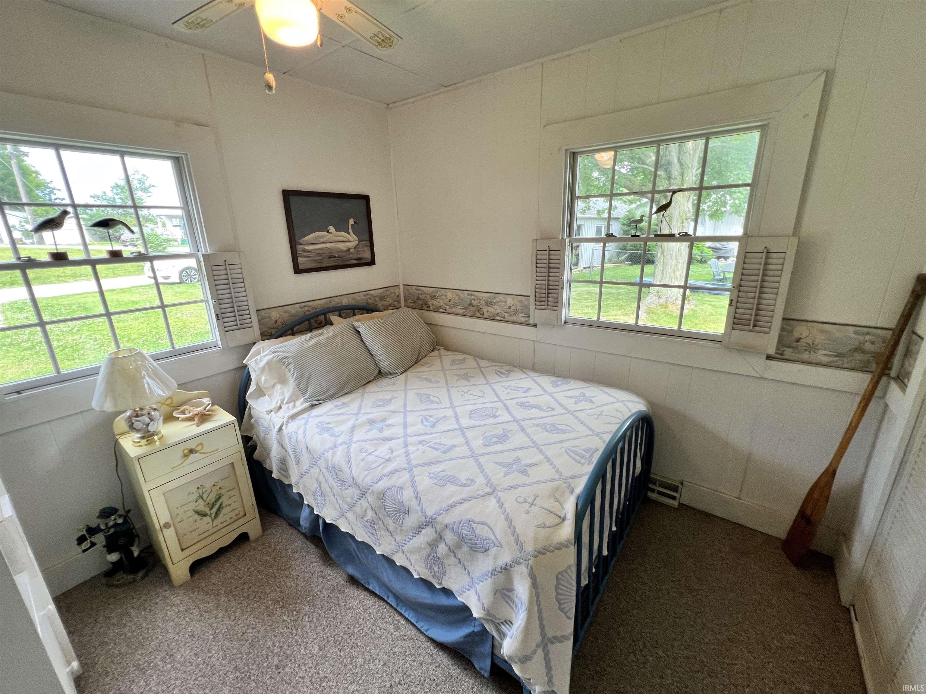 Bedroom featuring a ceiling fan with light fixture, two windows, and textured wall paneling