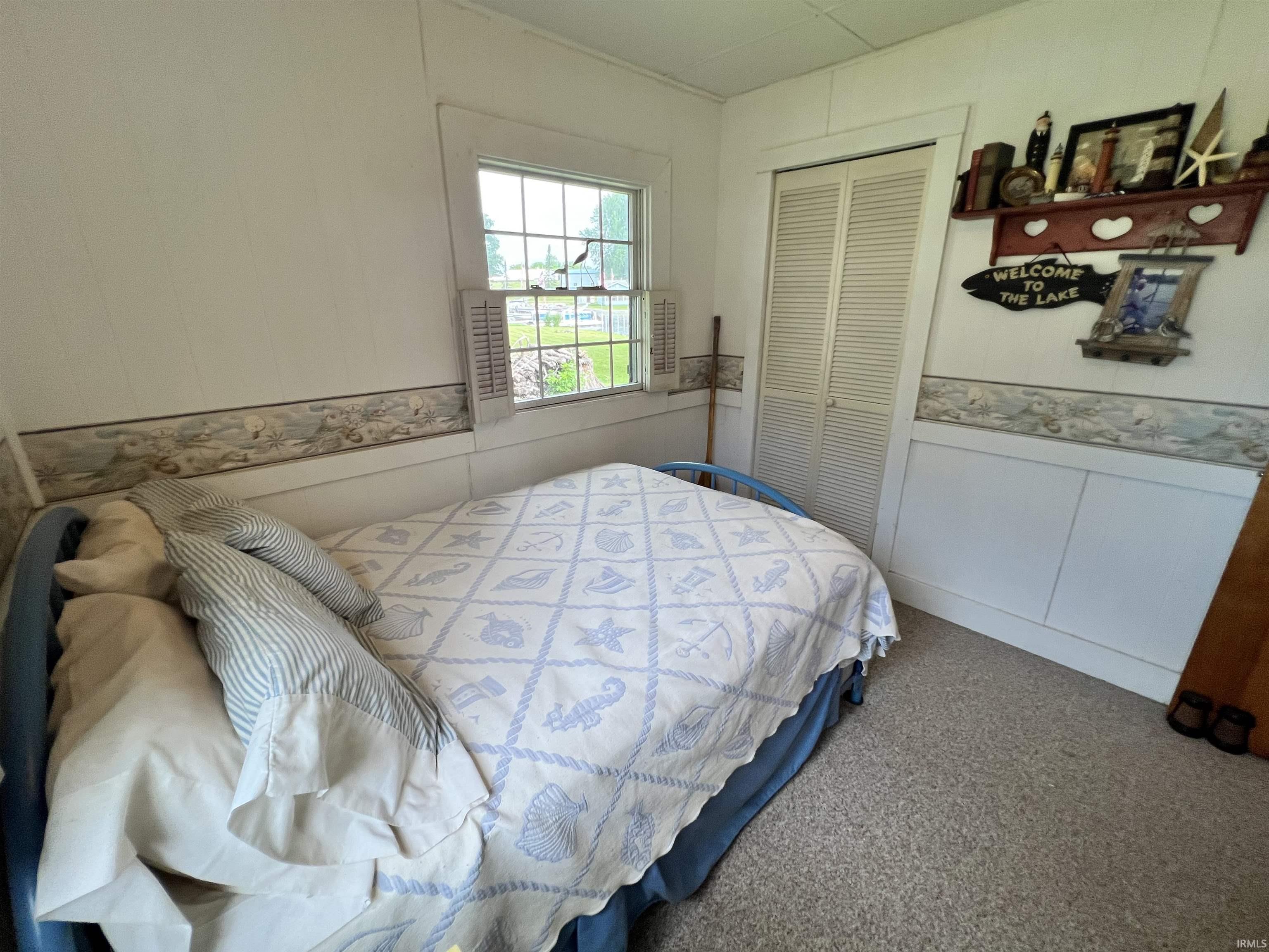 Room featuring a window with exterior views, white paneled walls, and light-colored carpeting