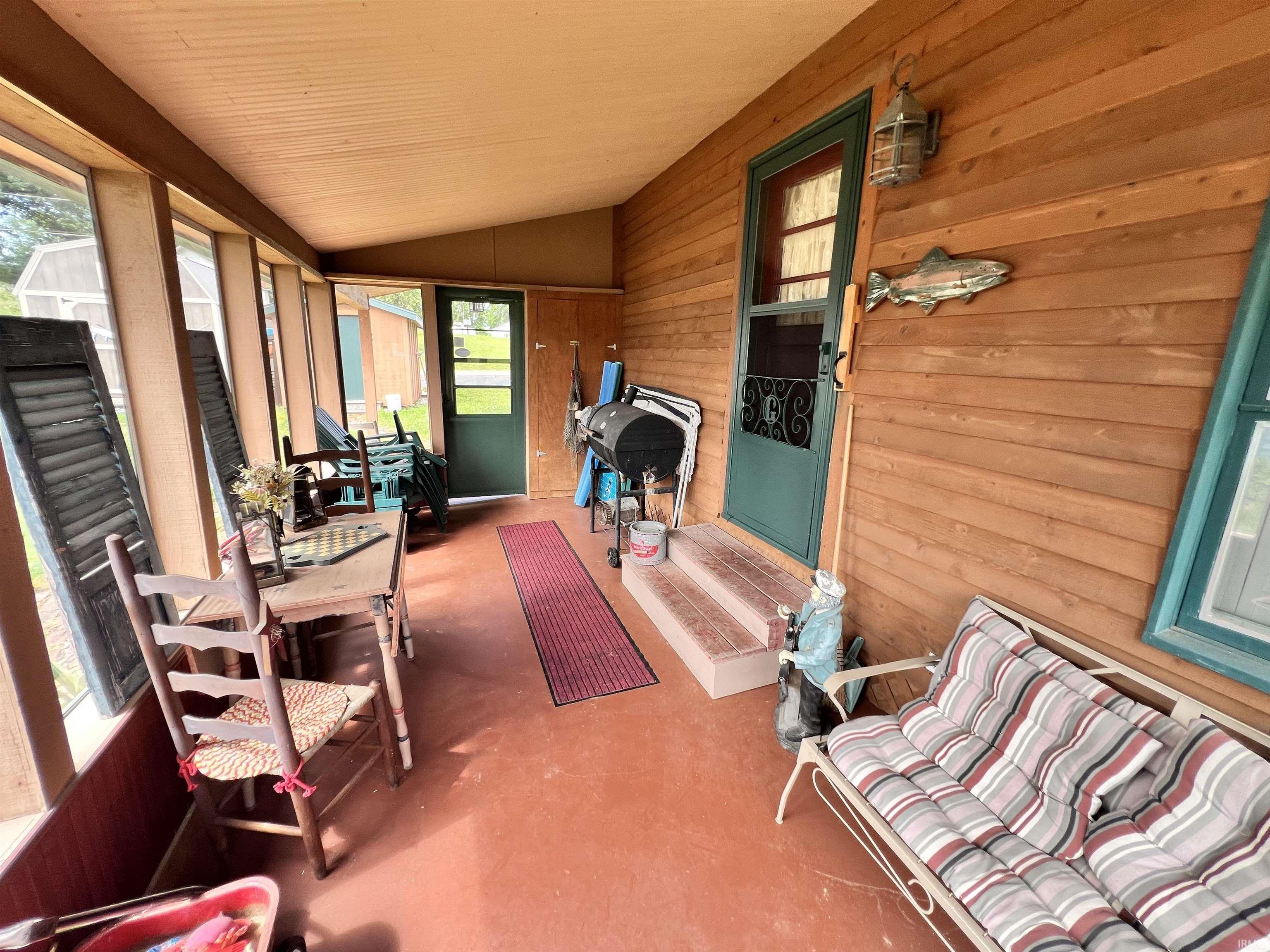 Enclosed porch featuring a sloped wood ceiling, screen panel walls, wood-finish siding, and a red-toned concrete floor