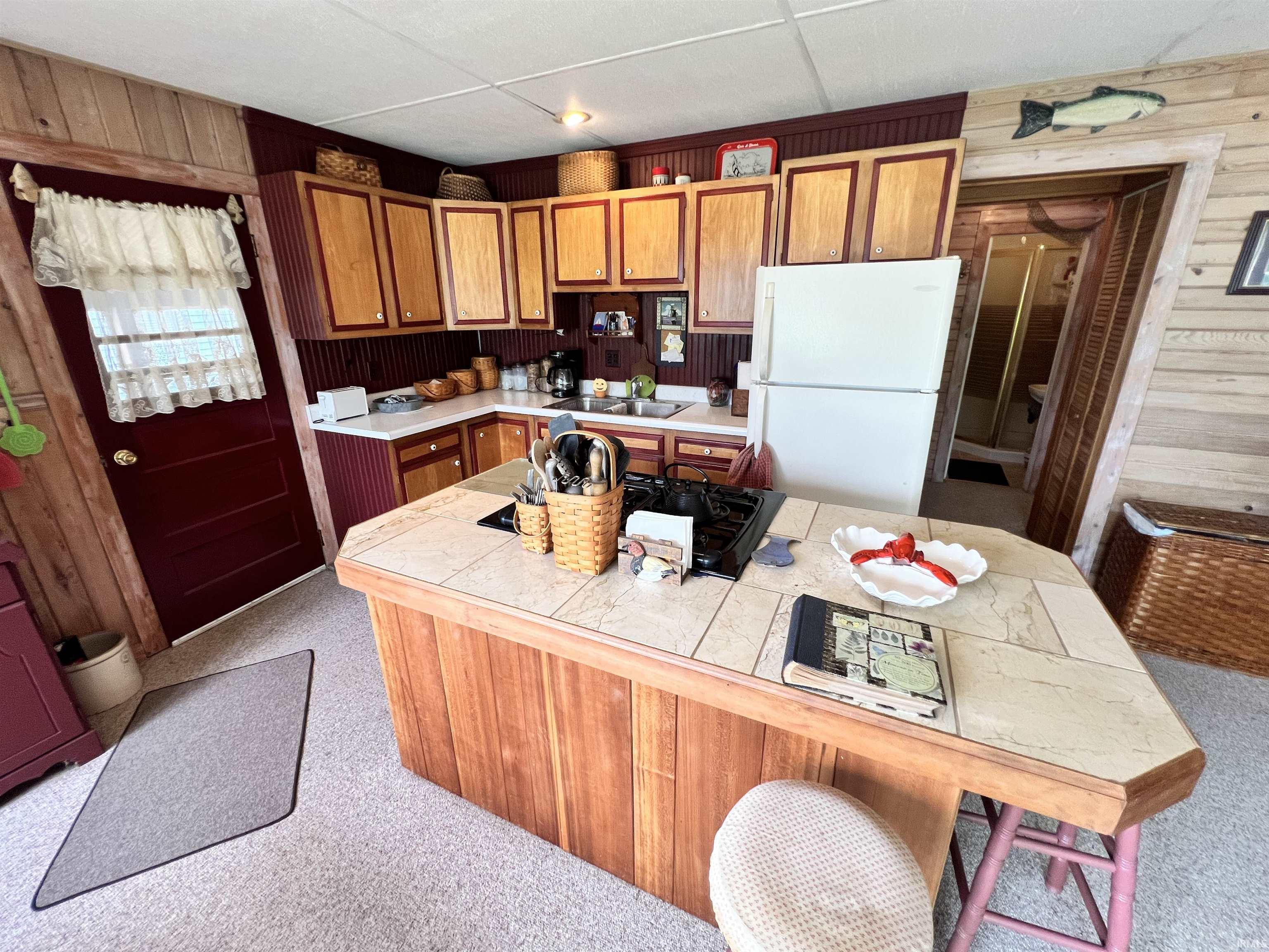Kitchen featuring wood-paneled island with tile countertop, wood cabinetry, and white appliances
