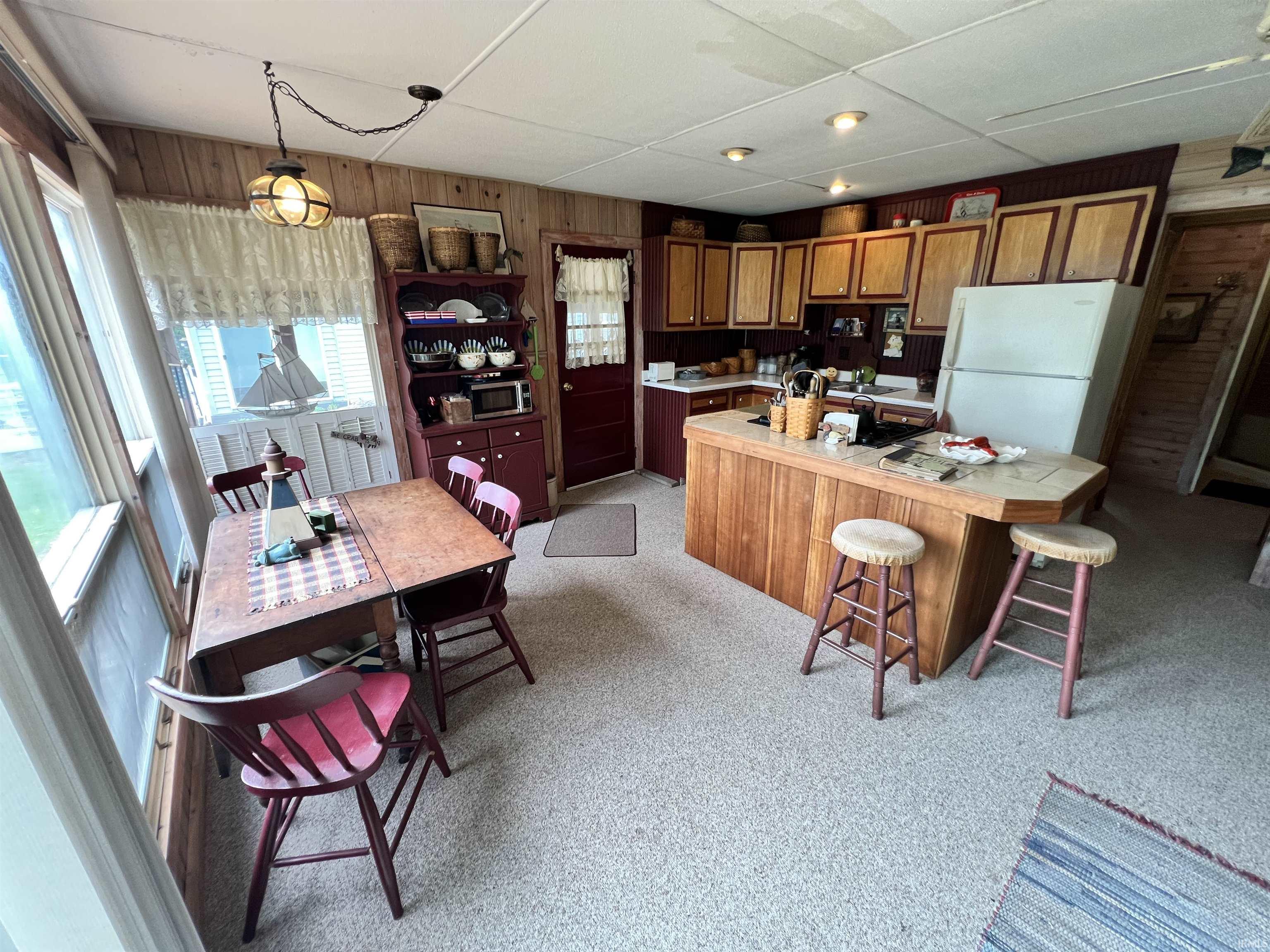 Open-concept kitchen and dining area featuring wood-finish cabinetry, a central island with a tiled countertop, and light-colored carpeting