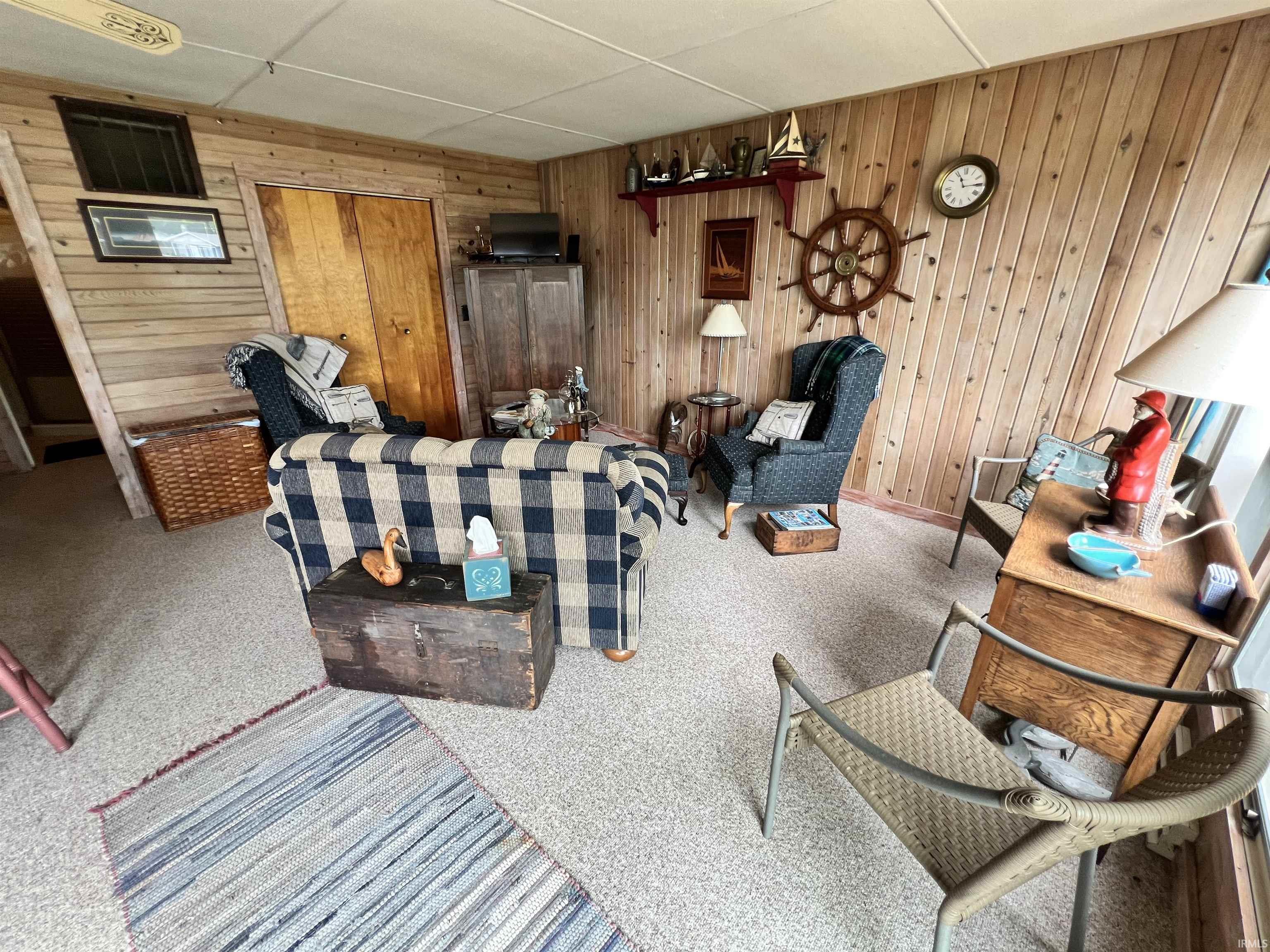 Room featuring wood-paneled walls, light-colored carpet flooring, and a flat ceiling
