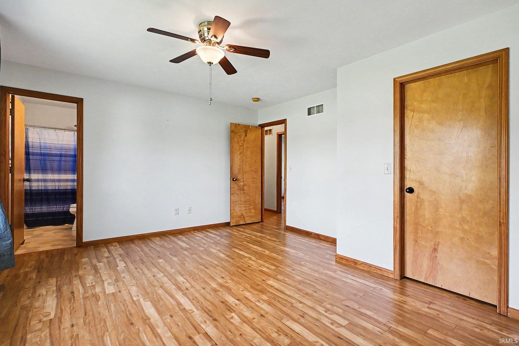 Spacious room featuring wood-finish flooring, light-colored walls, and a ceiling fan with ensuite