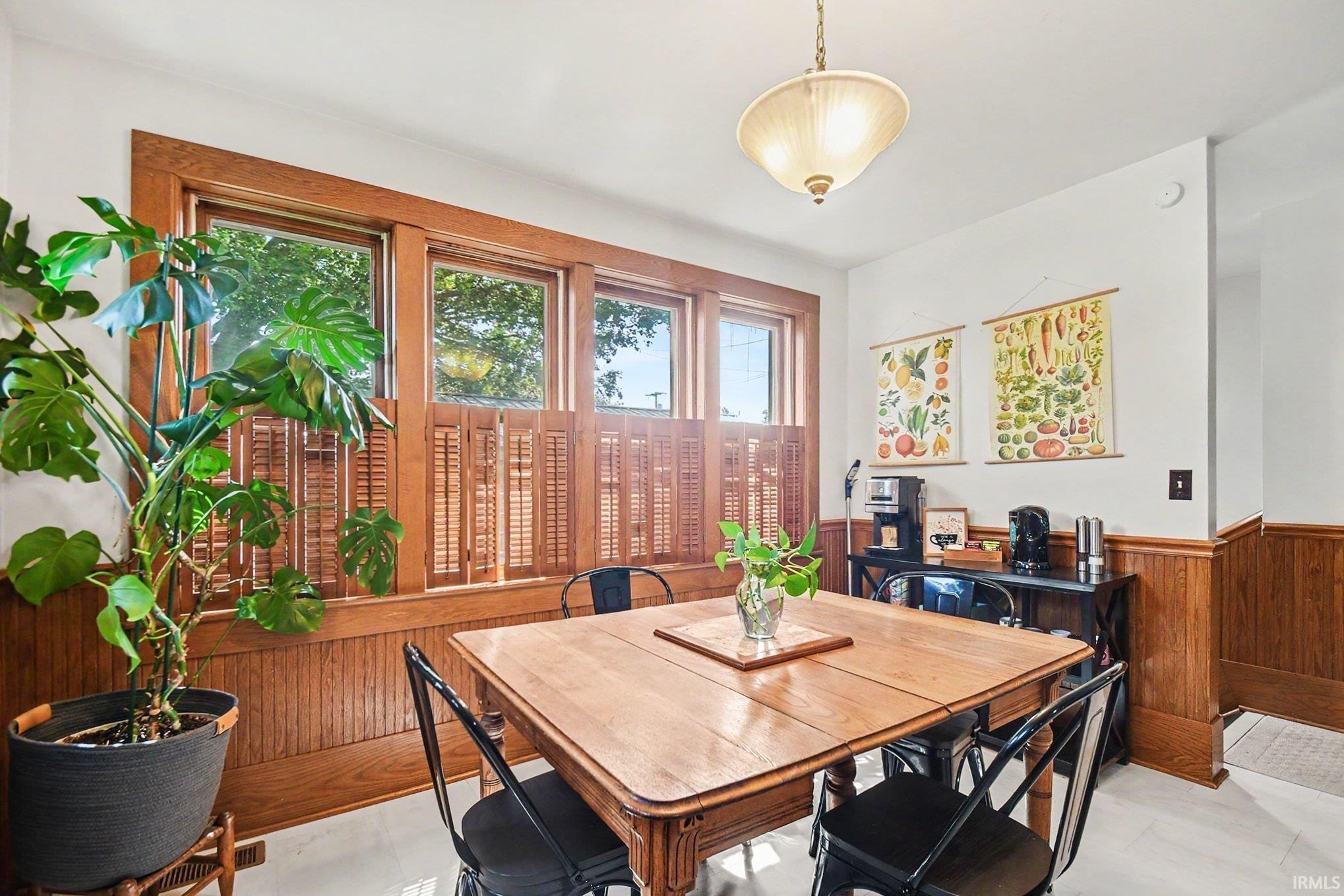Room featuring wood paneling, wood-frame windows with interior shutters, a wood-finish dining table, and light-tone flooring