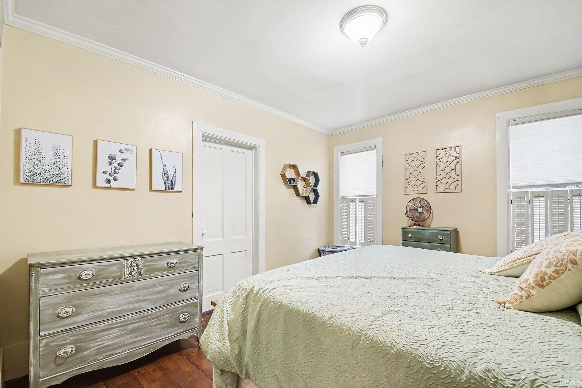 Bedroom featuring light yellow walls, white crown molding, and dark wood-finish flooring