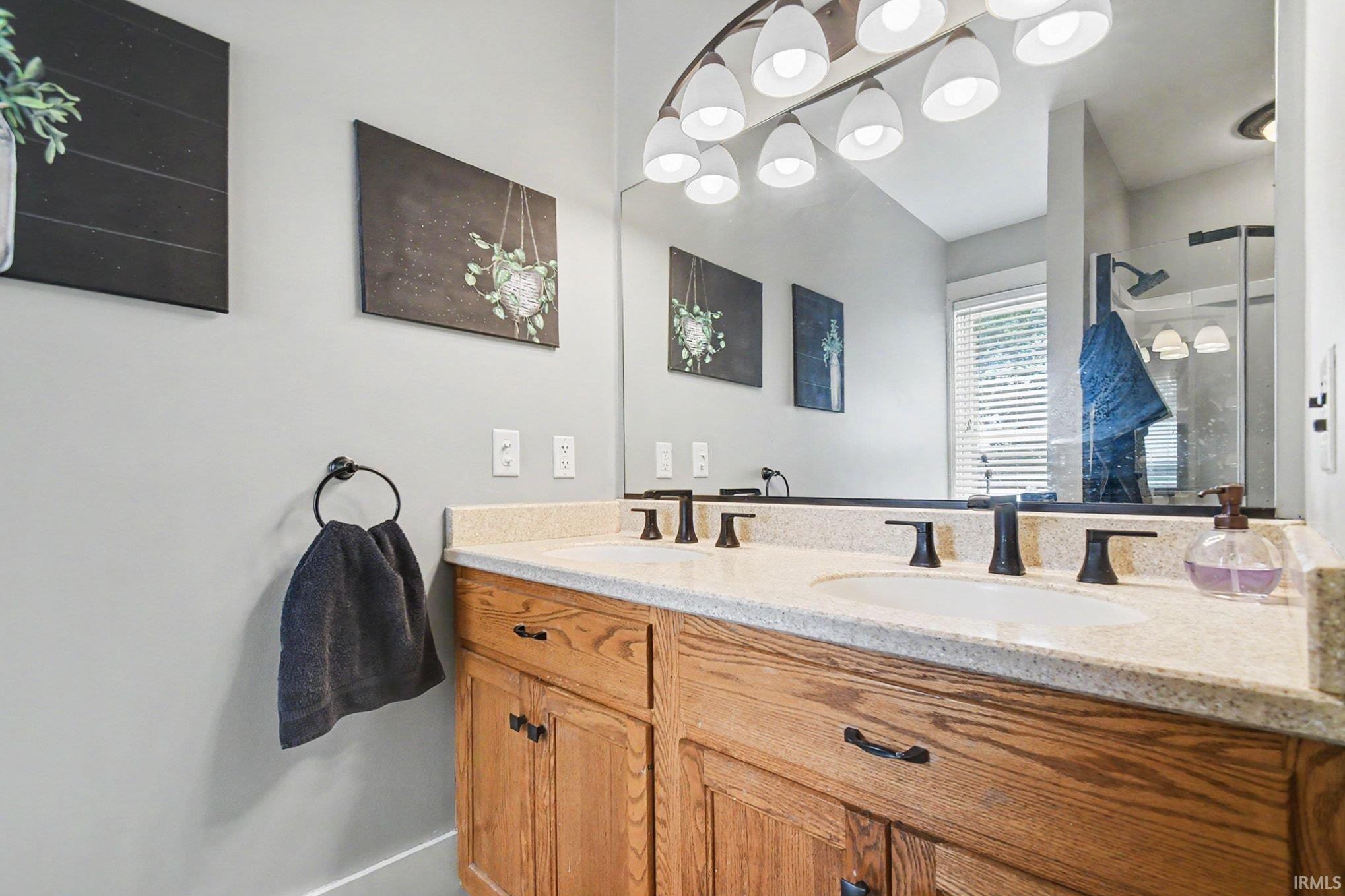 Dual vanity featuring wood-finish cabinetry, light-toned countertop, and matte black fixtures