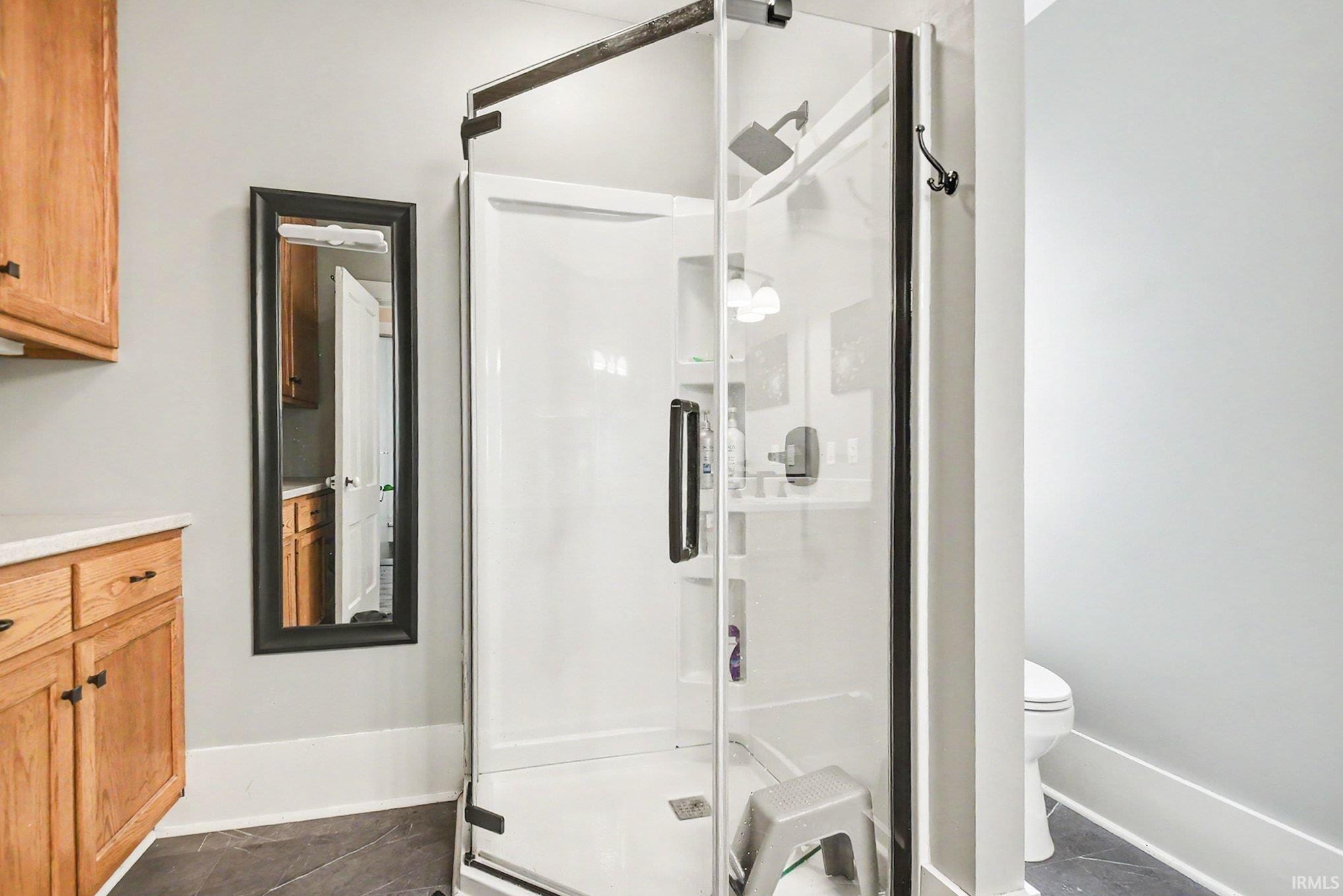 Glass-enclosed shower with a matte black frame, white shower base, and integrated shelving