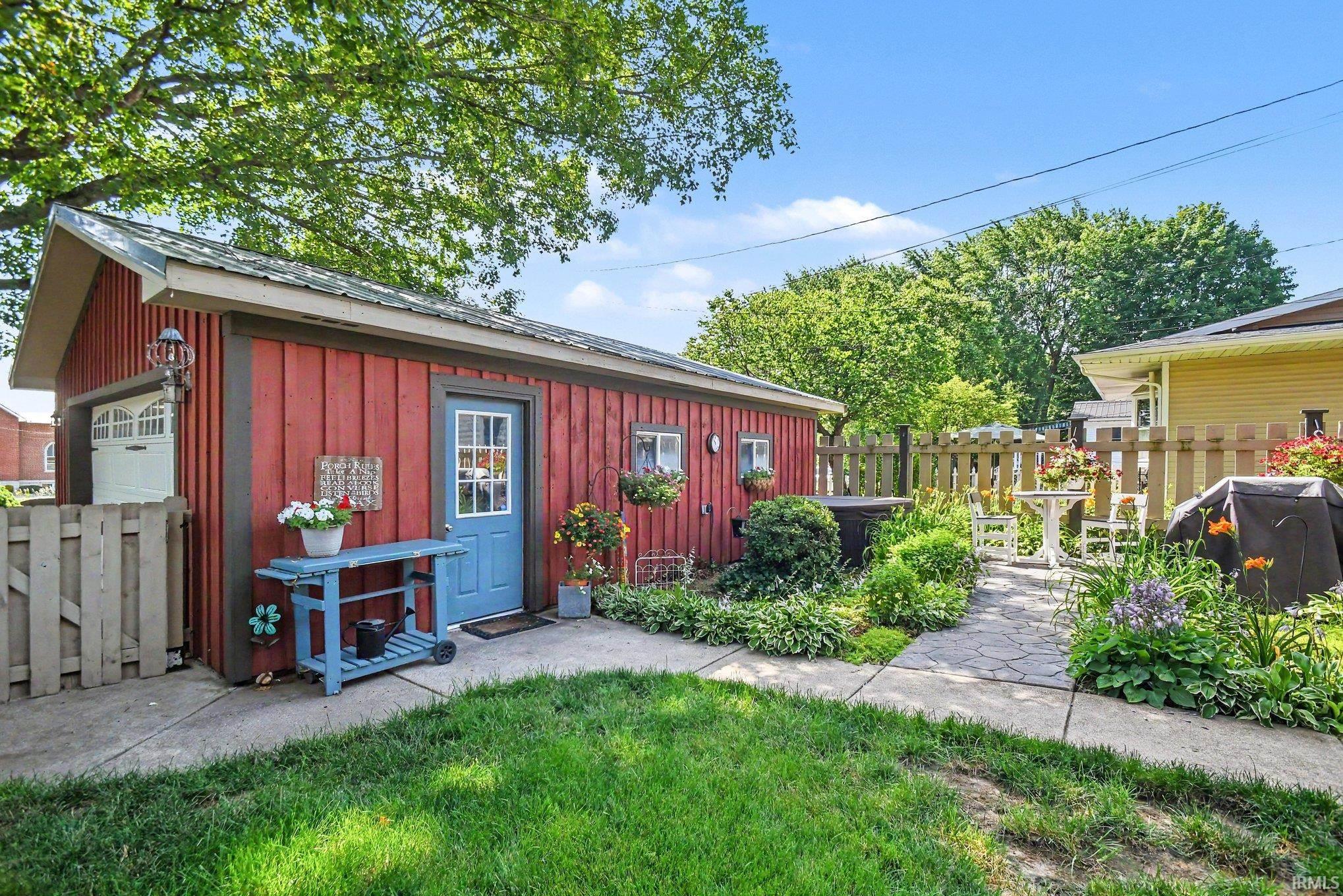 Detached red outbuilding featuring a blue entry door, an overhead garage door, and a stone paver pathway