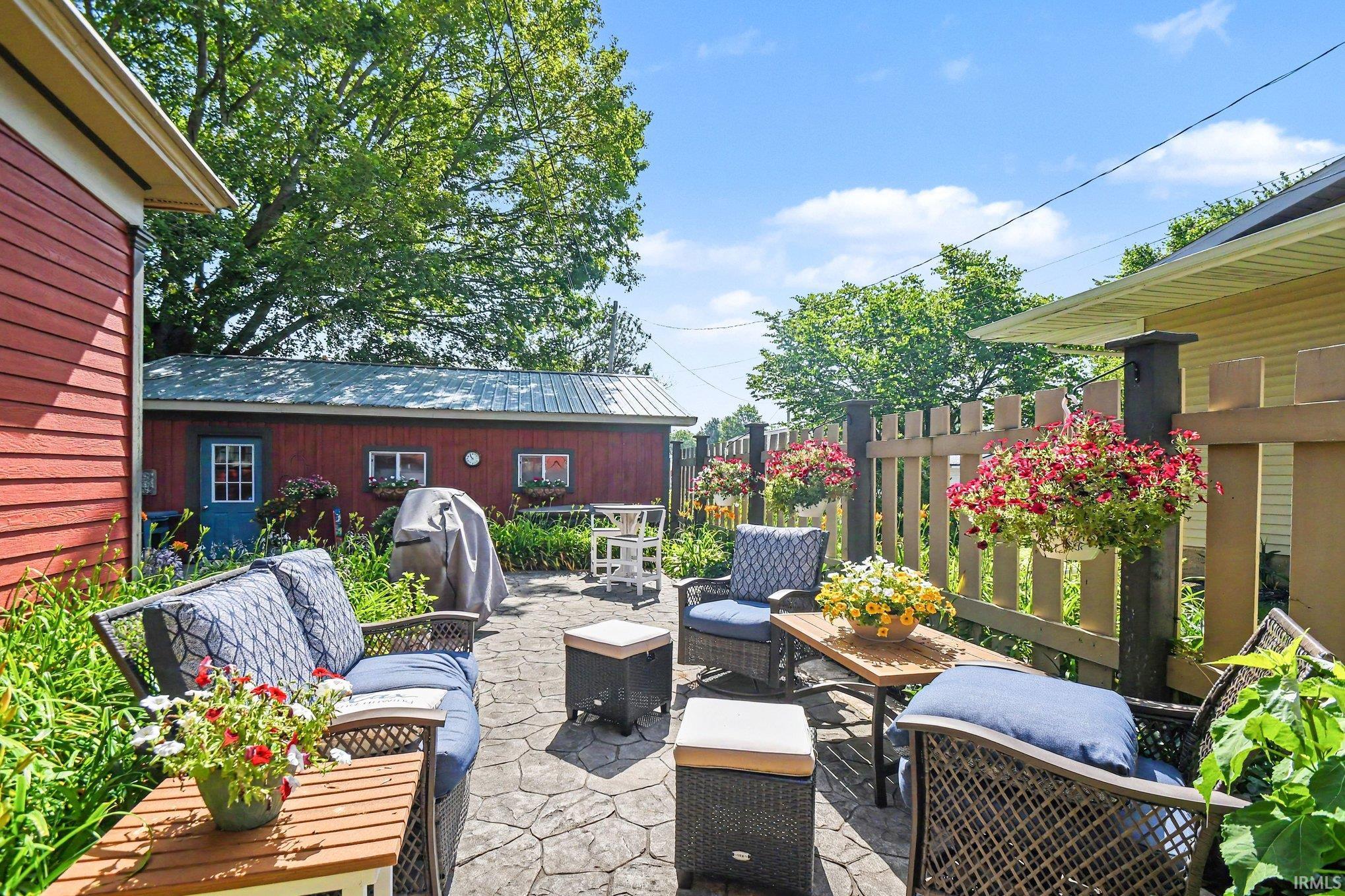 Exterior patio featuring stamped concrete, a wooden privacy fence, a red outbuilding with a metal roof, and an additional yellow-sided structure