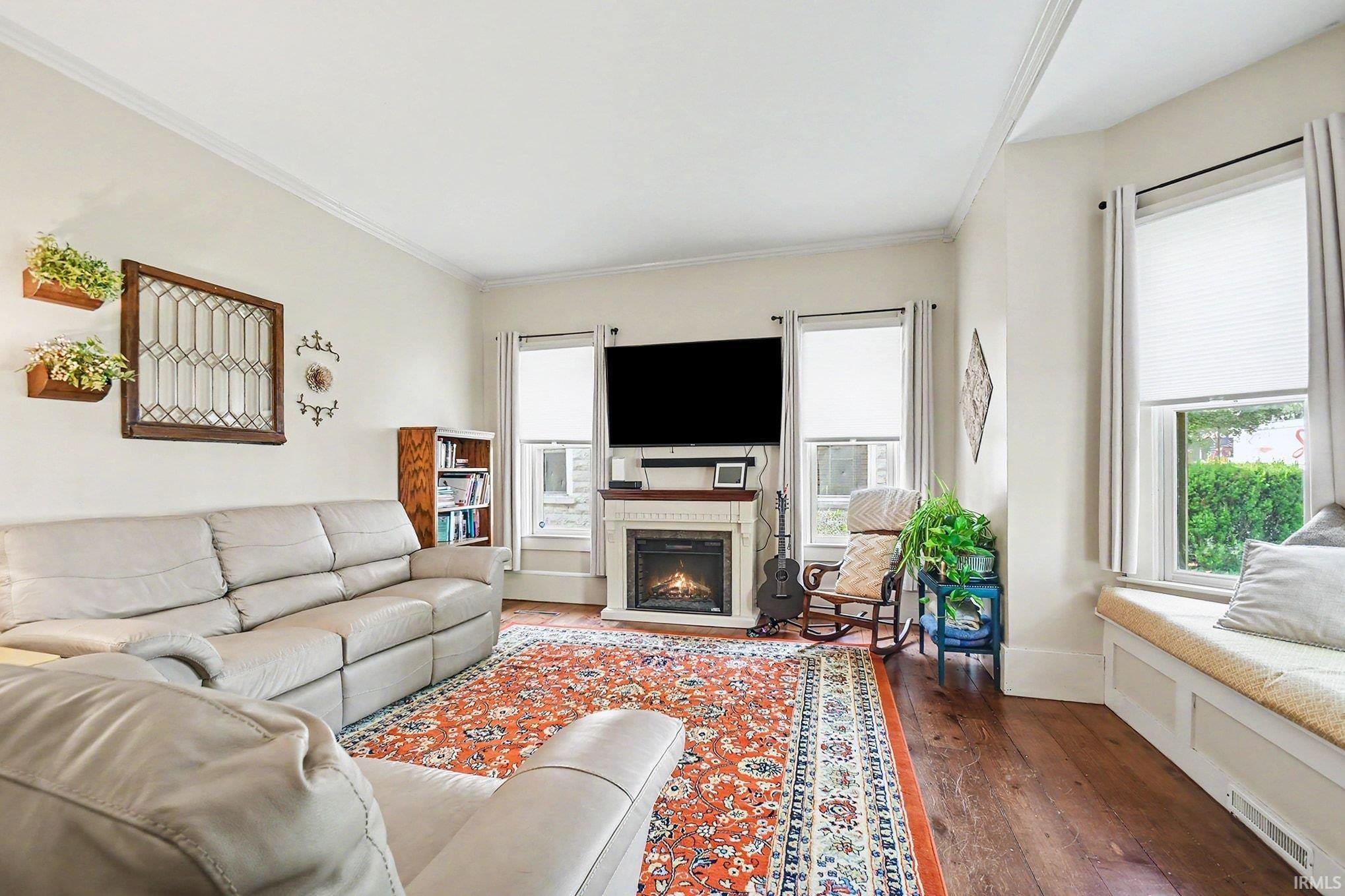 Living area featuring crown molding, dark wood-finish flooring, and a fireplace with a white mantel