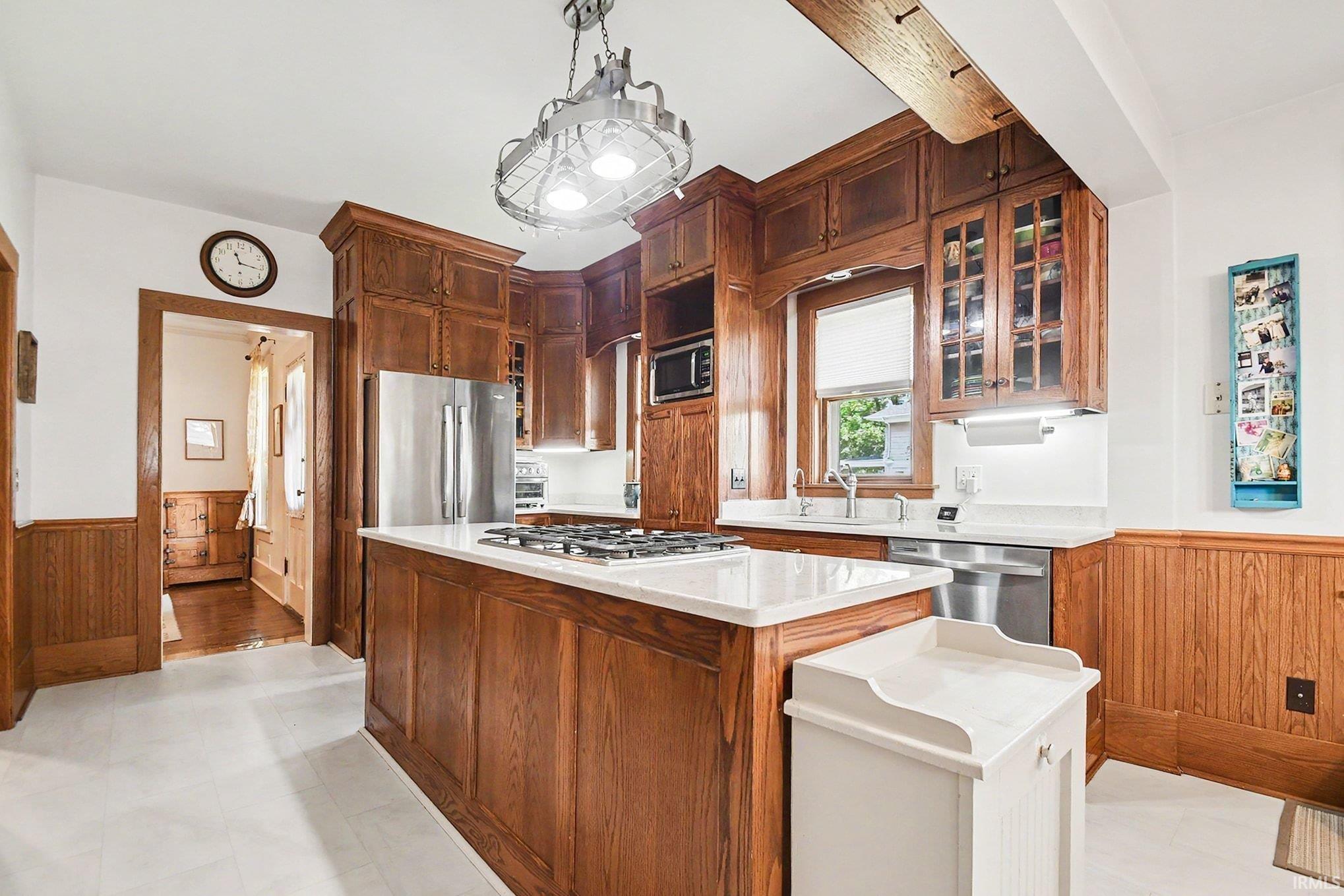 Kitchen featuring wood cabinetry, stainless steel appliances, a center island with cooktop, white countertops, and beadboard paneling