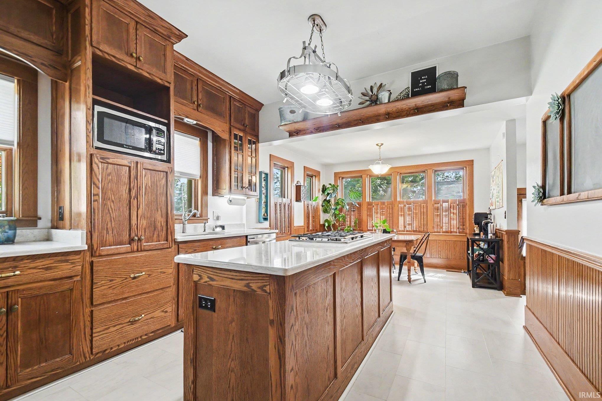 Kitchen featuring extensive wood cabinetry, white countertops, built-in microwave, integrated sink, and an island with cooktop