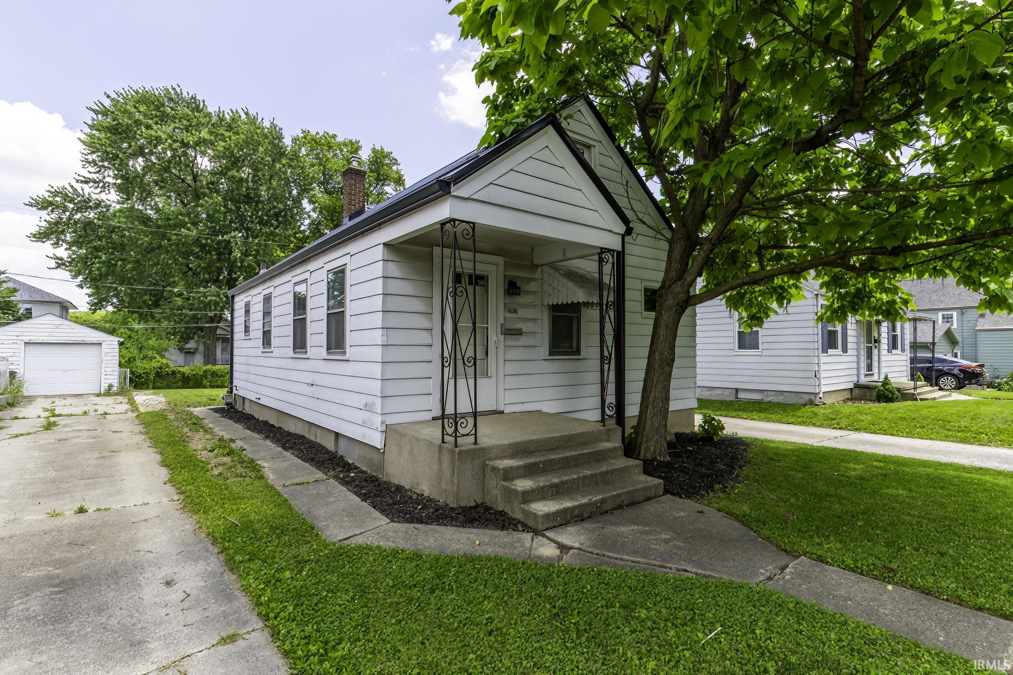 White siding exterior featuring a covered porch with decorative wrought iron columns, concrete steps, and a concrete driveway