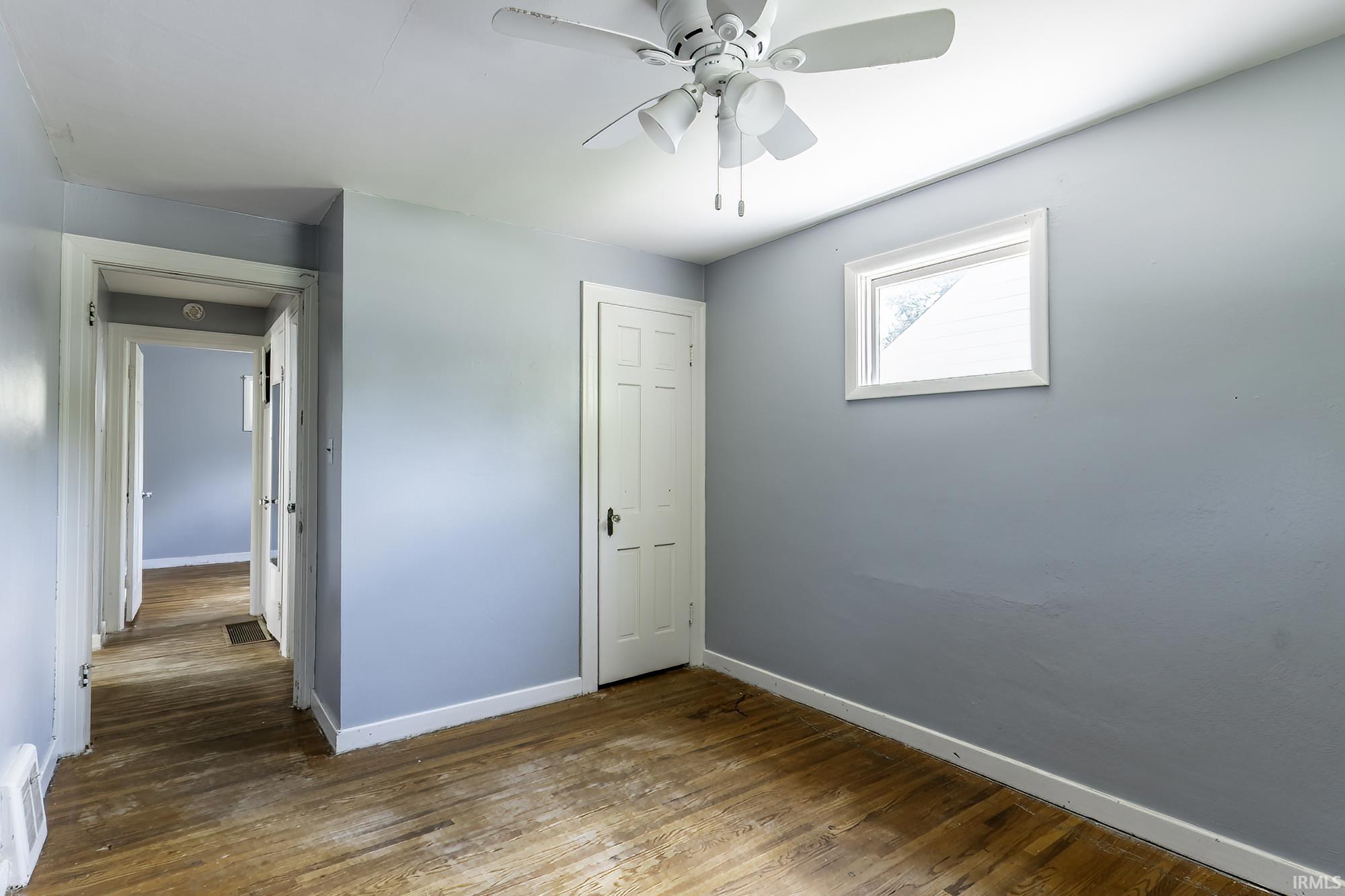 Bedroom featuring a window, ceiling fan with light fixture, wood-finish flooring, and light blue walls