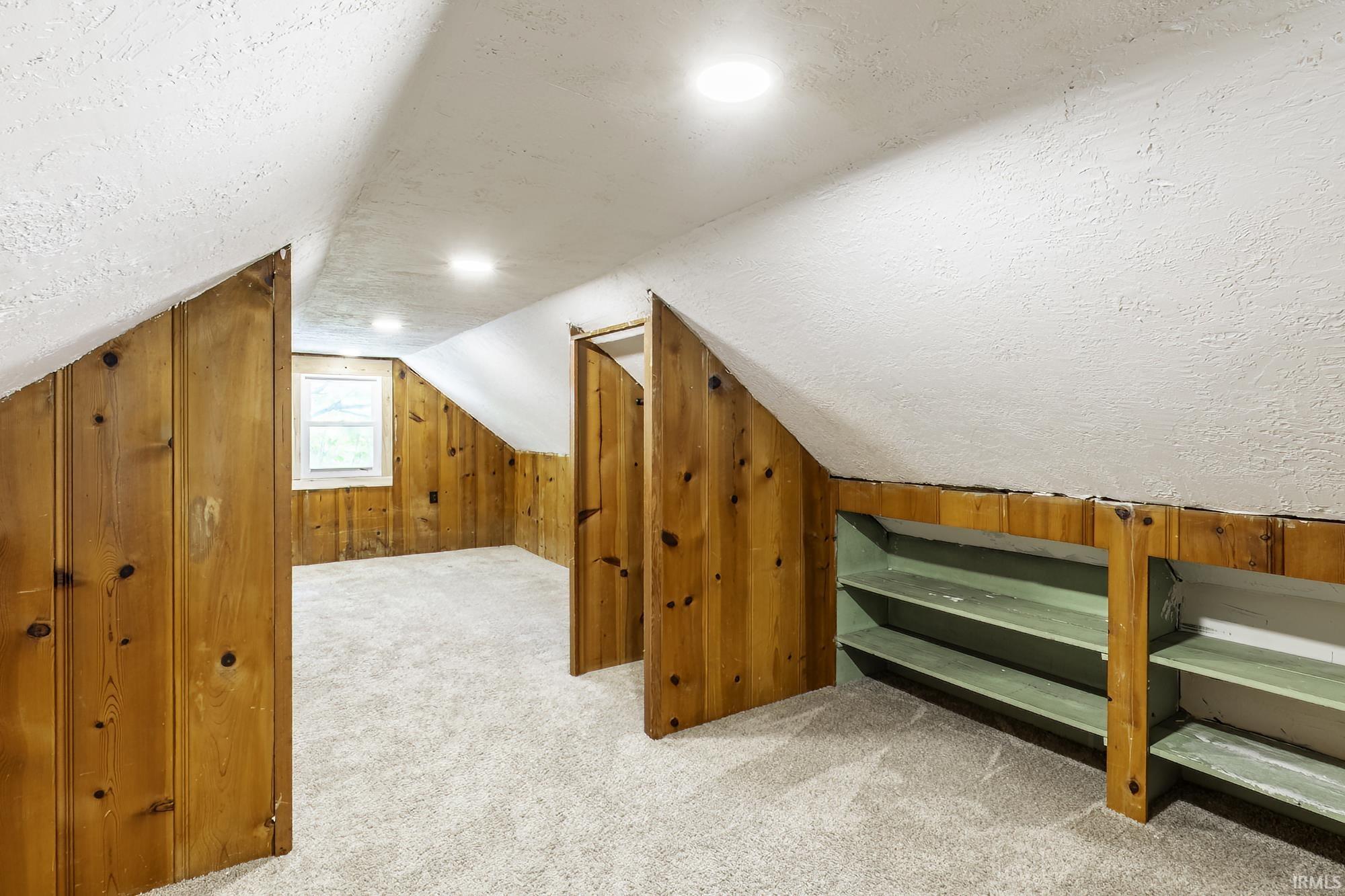Versatile attic space featuring recessed lighting, a window for natural light, wood paneling, and built-in shelving