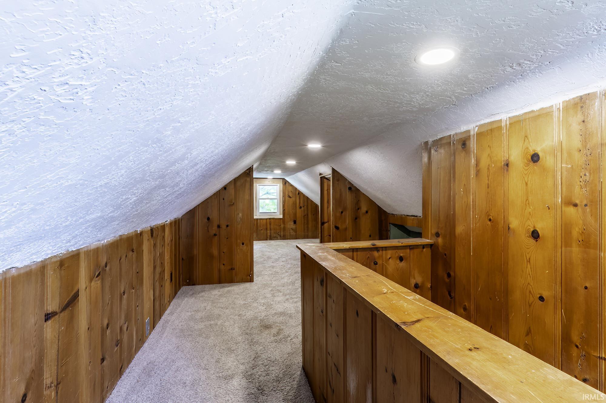 Attic space featuring wood-paneled walls, light-colored carpeting, recessed lighting, and a single window