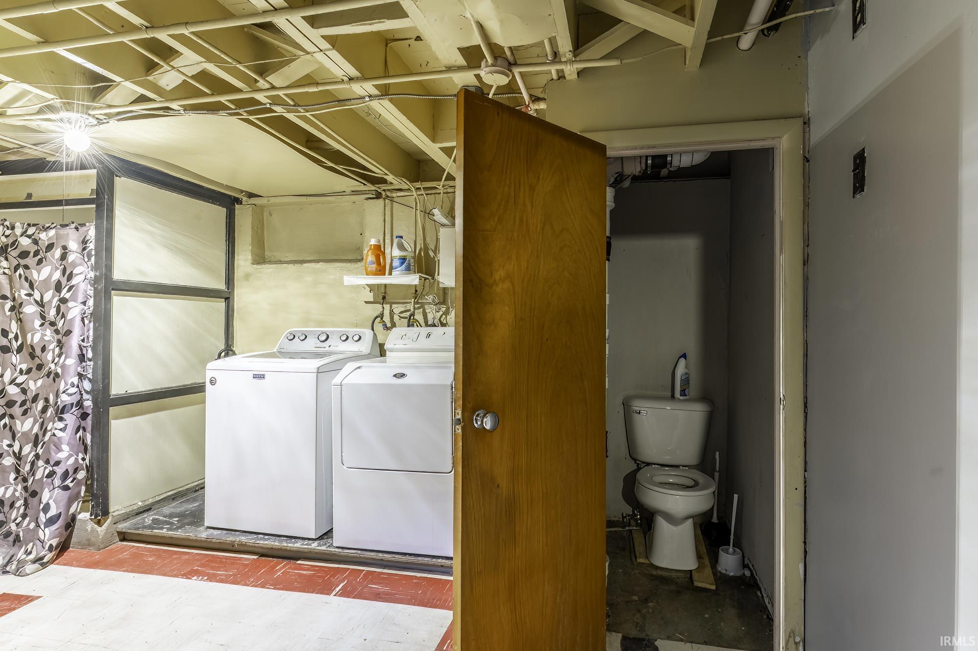 Dedicated laundry area featuring a washer and dryer, exposed ceiling joists, and a partial privacy wall